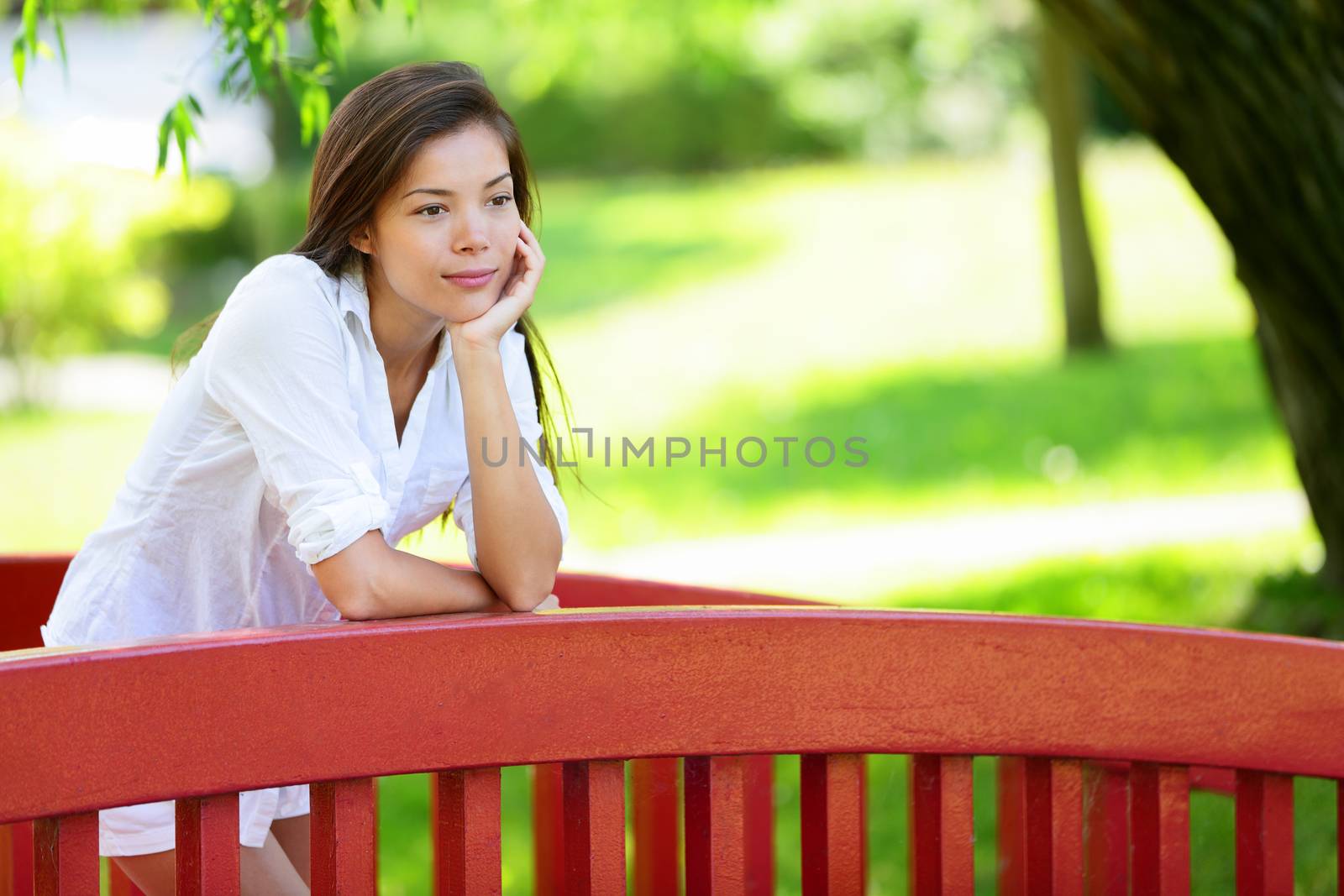 Thoughtful young woman pensive at park. Beautiful female leaning with hand on chin. Asian chinese woman calm and relaxing in summer outdoors.