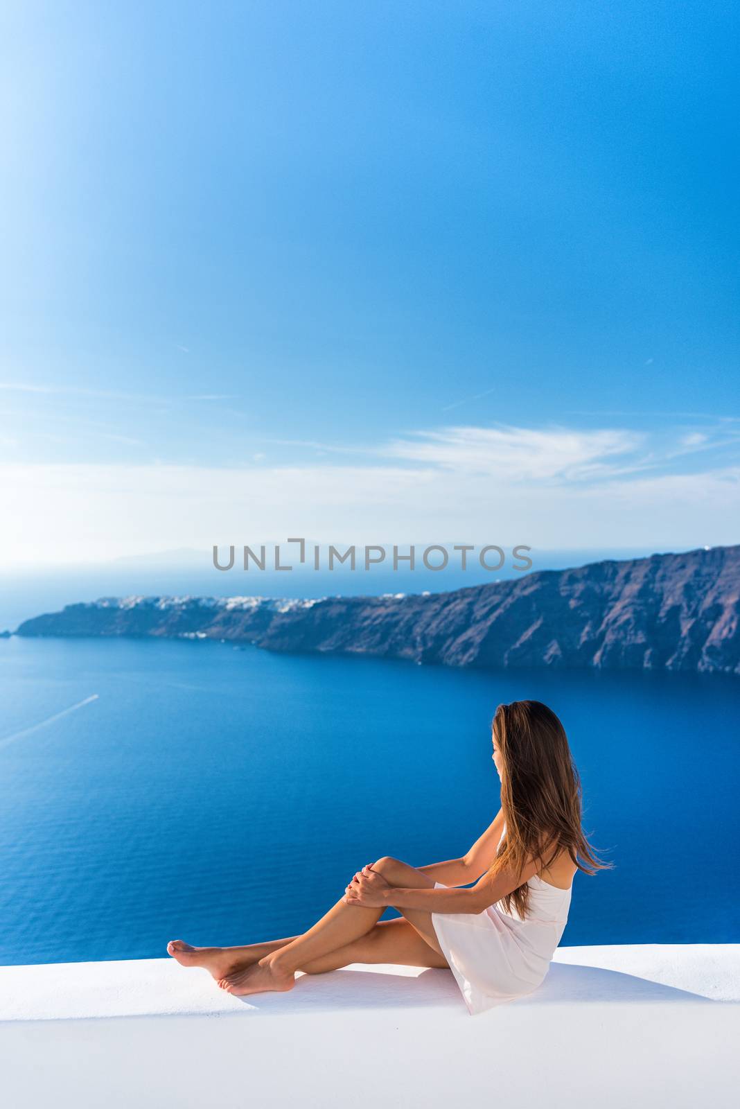 Luxury travel vacation Europe tourist woman relaxing at fancy hotel resort balcony in greek Santorini island, Greece with view over the Mediterranean Sea and Oia. Elegant girl living jetset lifestyle by Maridav