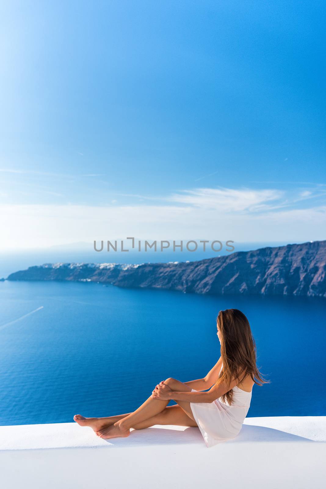 Luxury travel vacation Europe tourist woman relaxing at fancy hotel resort balcony in greek Santorini island, Greece with view over the Mediterranean Sea and Oia. Elegant girl living jetset lifestyle.