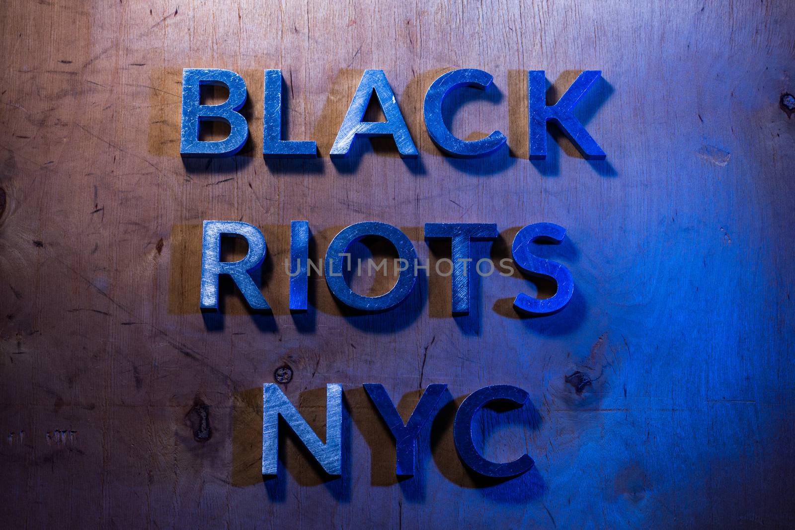 The words black riots NYC laid with metal letters on flat plywood surface under white and blue police lights. Concept of night disorder in New York City.