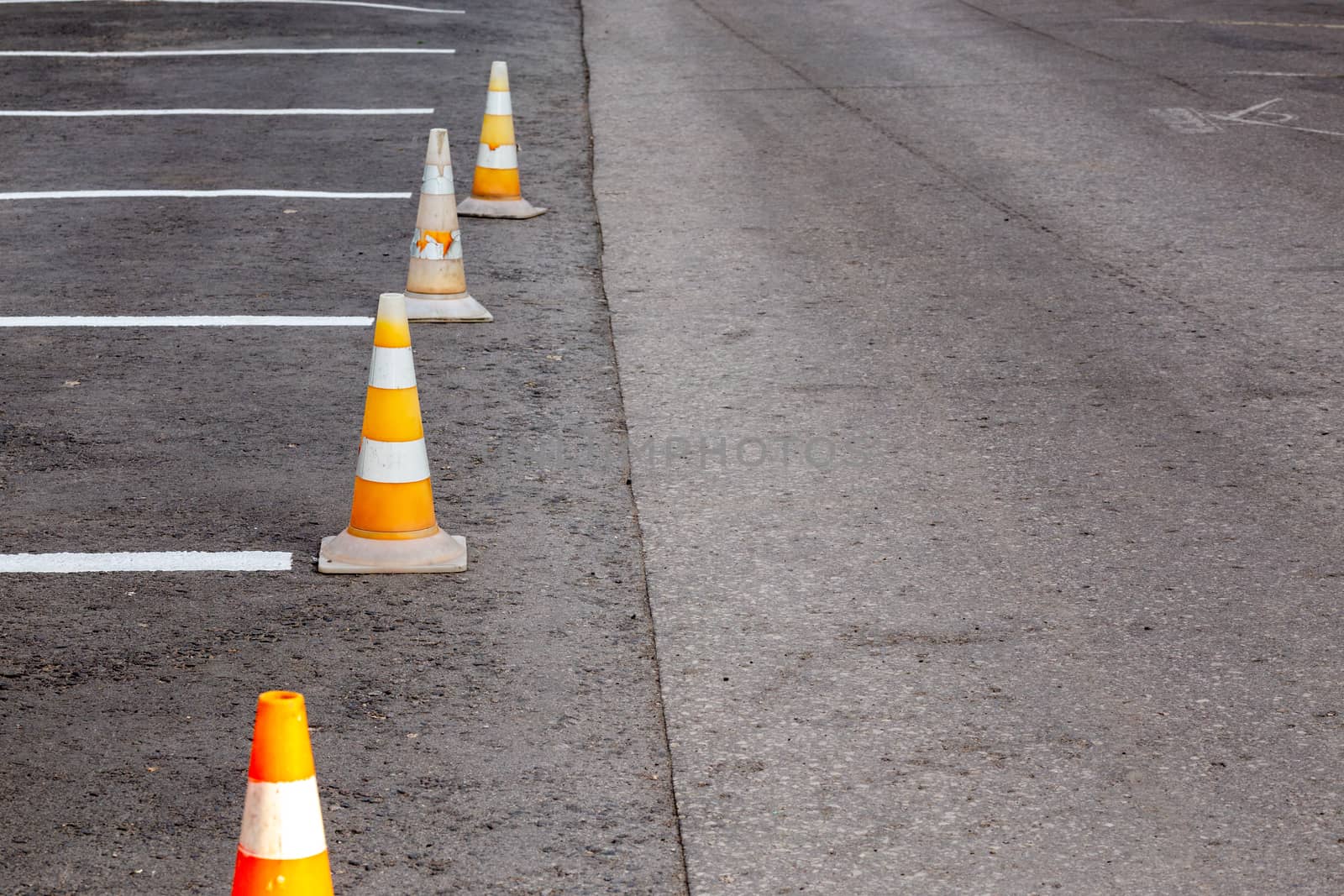 Orange road cones on a asphelt driving area with white lines, close-up with selective focus and backgropund blur.