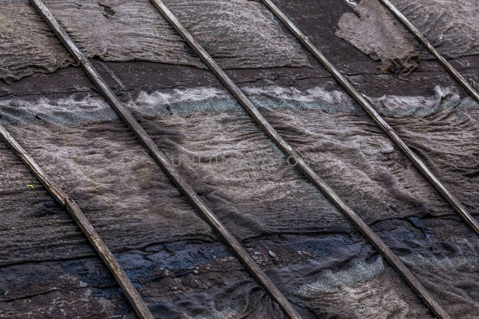 old rotten black ruberoid shed gable roofing close-up with selective focus and blur.