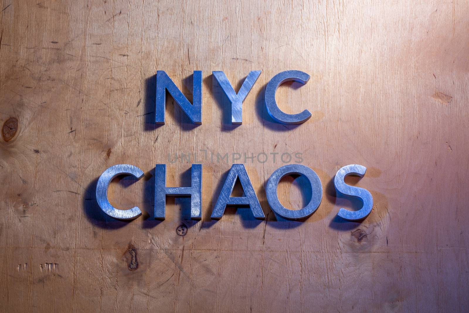 The words NYC chaos laid with metal letters on flat plywood surface under white and blue police lights. Concept of night disorder in New York City.