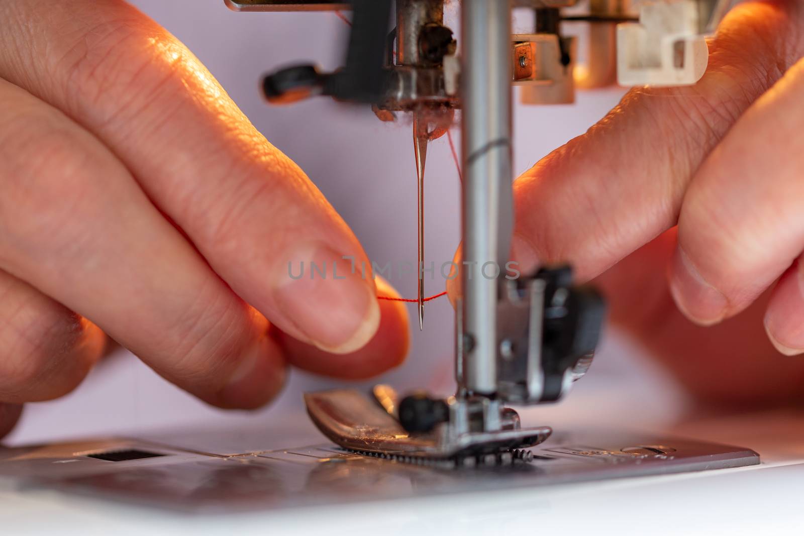 elder woman fingers inserting a red thread into a sewing machine needle, close-up with selective focus
