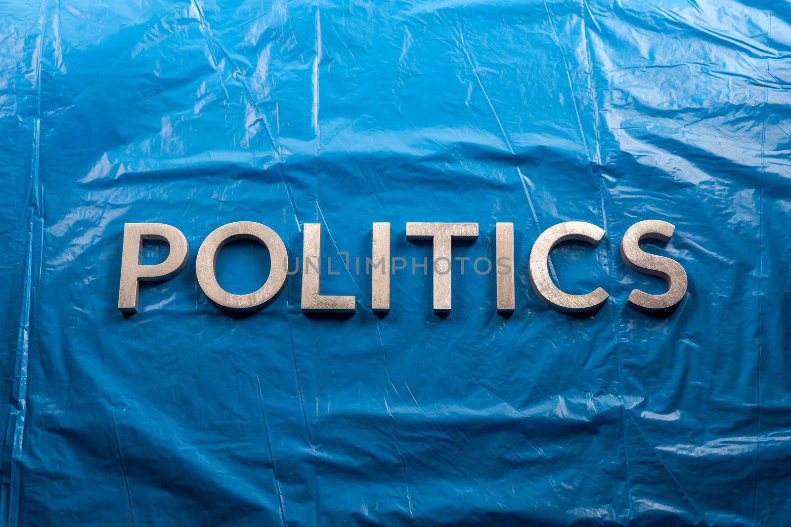 the word politics laid with silver aluminium letters over crumpled plastic blue film background - in center of picture.