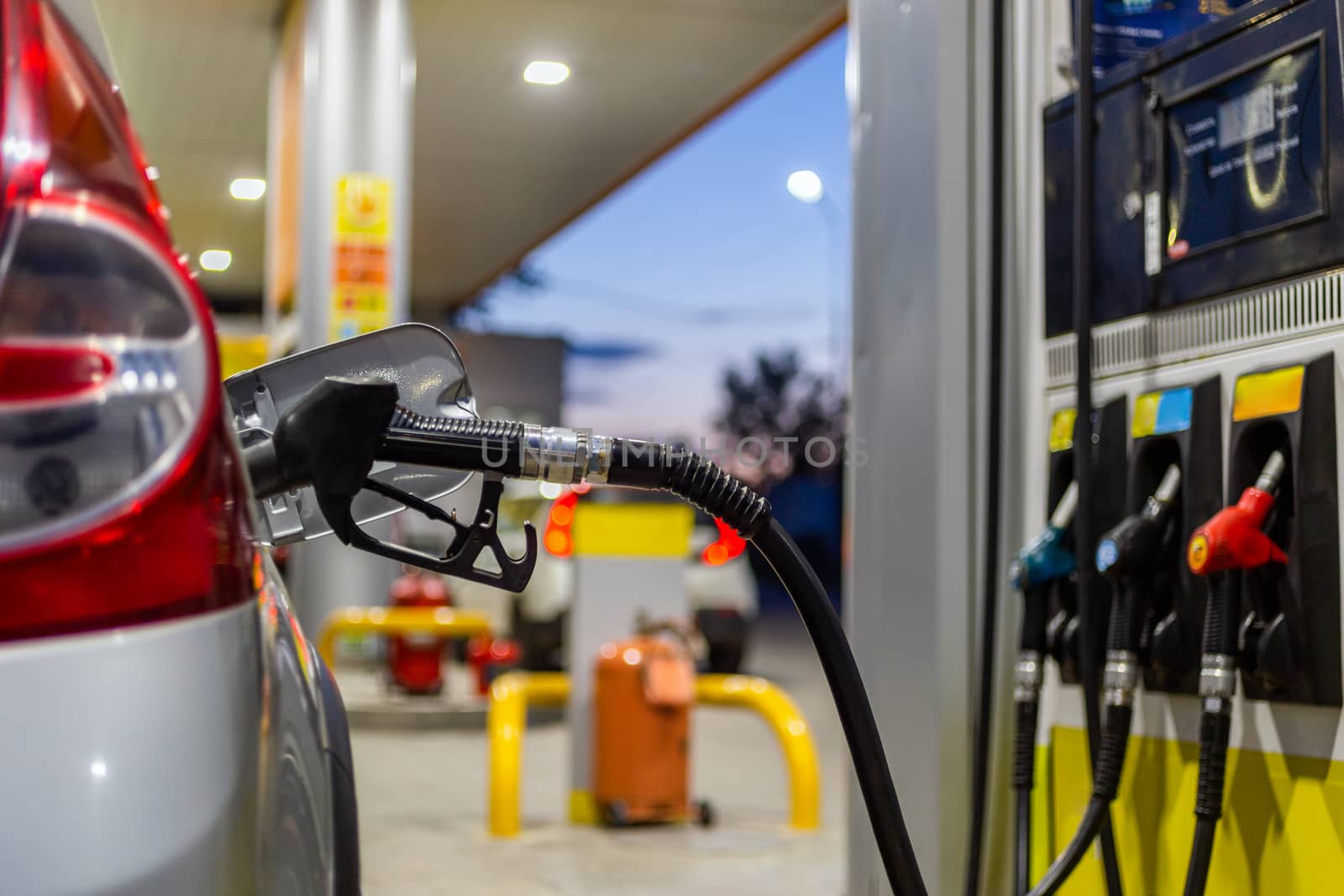 silver car refueling on night gas station - close-up with selective focus and blurry background.
