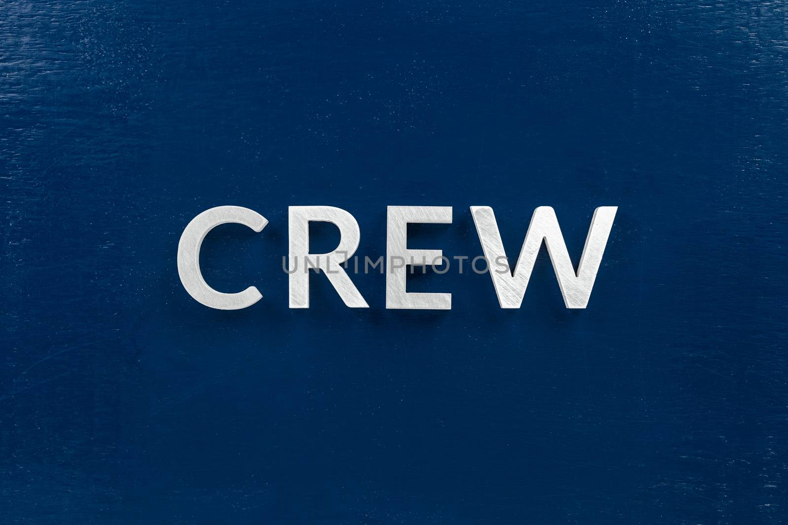 the word crew laid with brushed white metal letters over flat blue board - in center of picture, directly above perspective