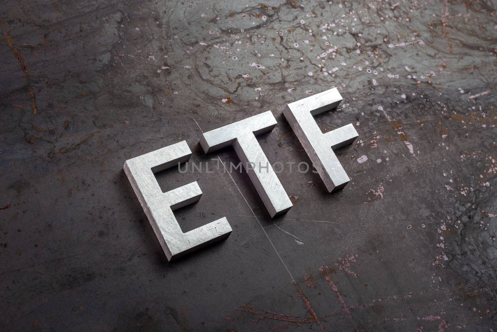 the abbreviation word etf - Exchange Traded Fund - laid with silver letters on raw rusted steel sheet surface in slanted diagonal perspective.