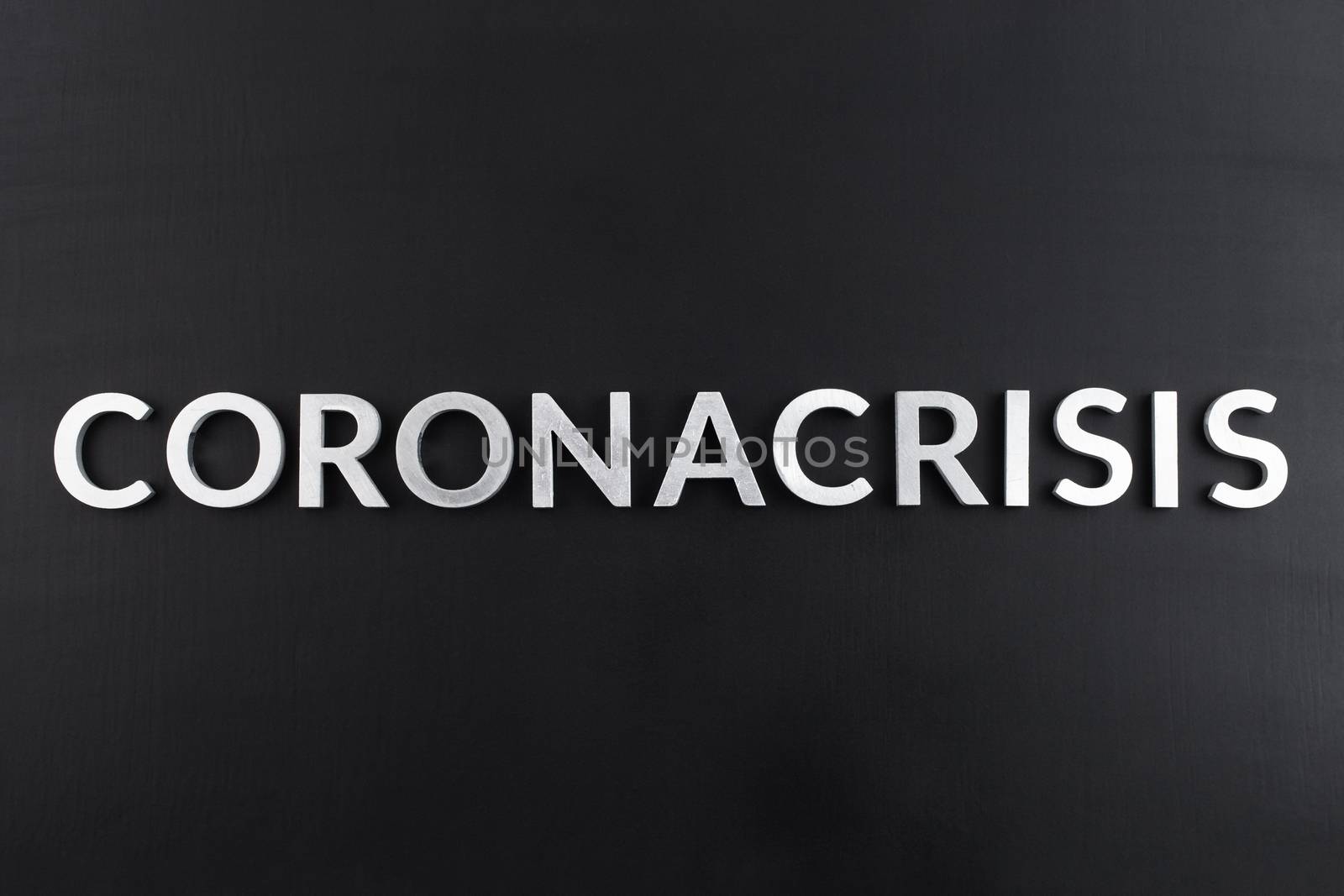 the word coronacrisis laid with white brushed metal letters on flat black surface in directly above perspective