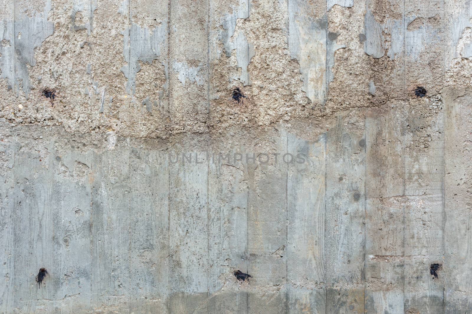 an outdoor thick rough gray concrete wall with visible imprints of wooden planks, twice filled