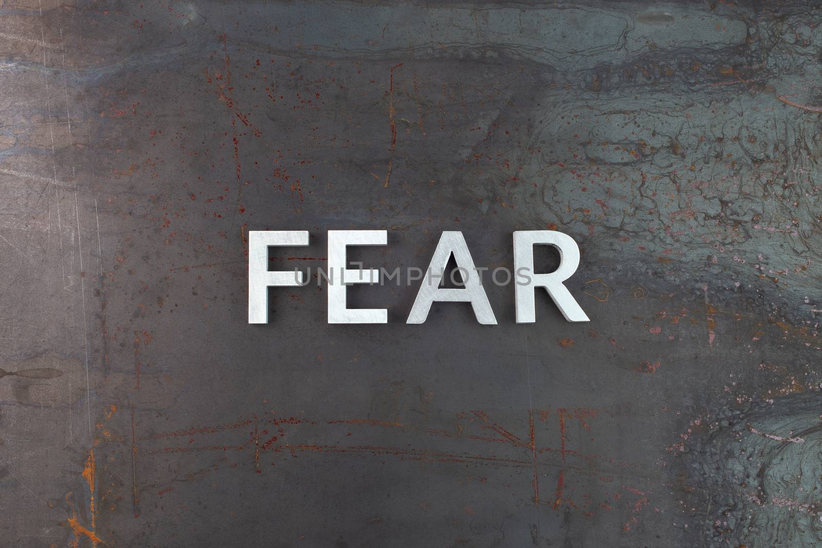 the word fear laid with silver letters on raw rusted steel sheet surface in flat lay composition