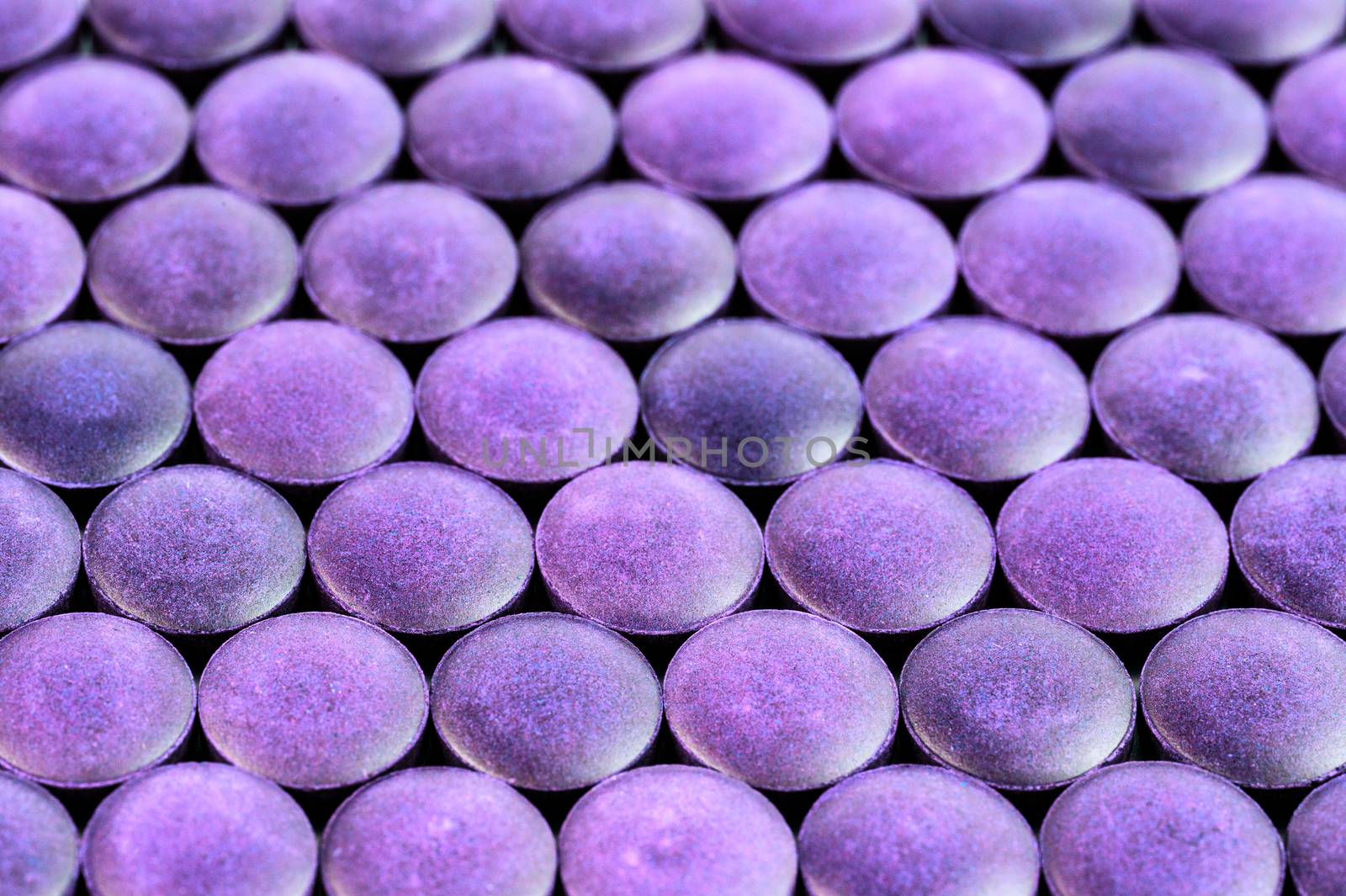 close-up background of many violet organic compacted powder tablets laid tight in one layer on flat surface.