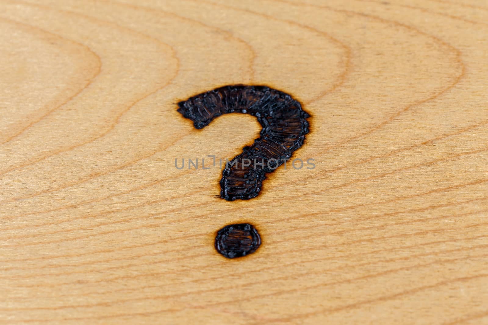 question mark drawn with handheld woodburner on bright flat wooden surface with selective focus and background blur
