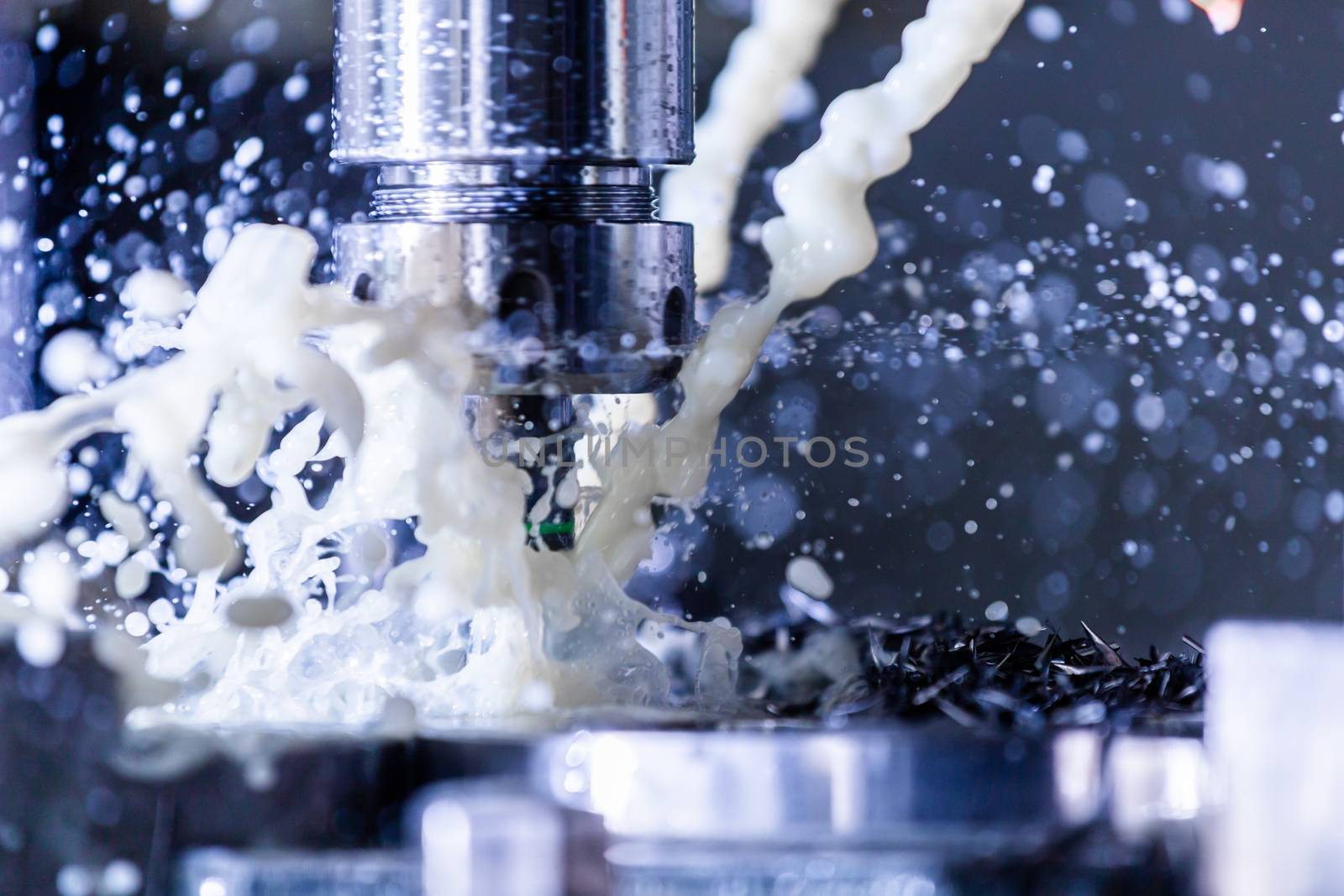 A process of vertical cnc steel milling with external water coolant streams, splashes and a lot of metal chips. Fast shutter speed for motion freezing.