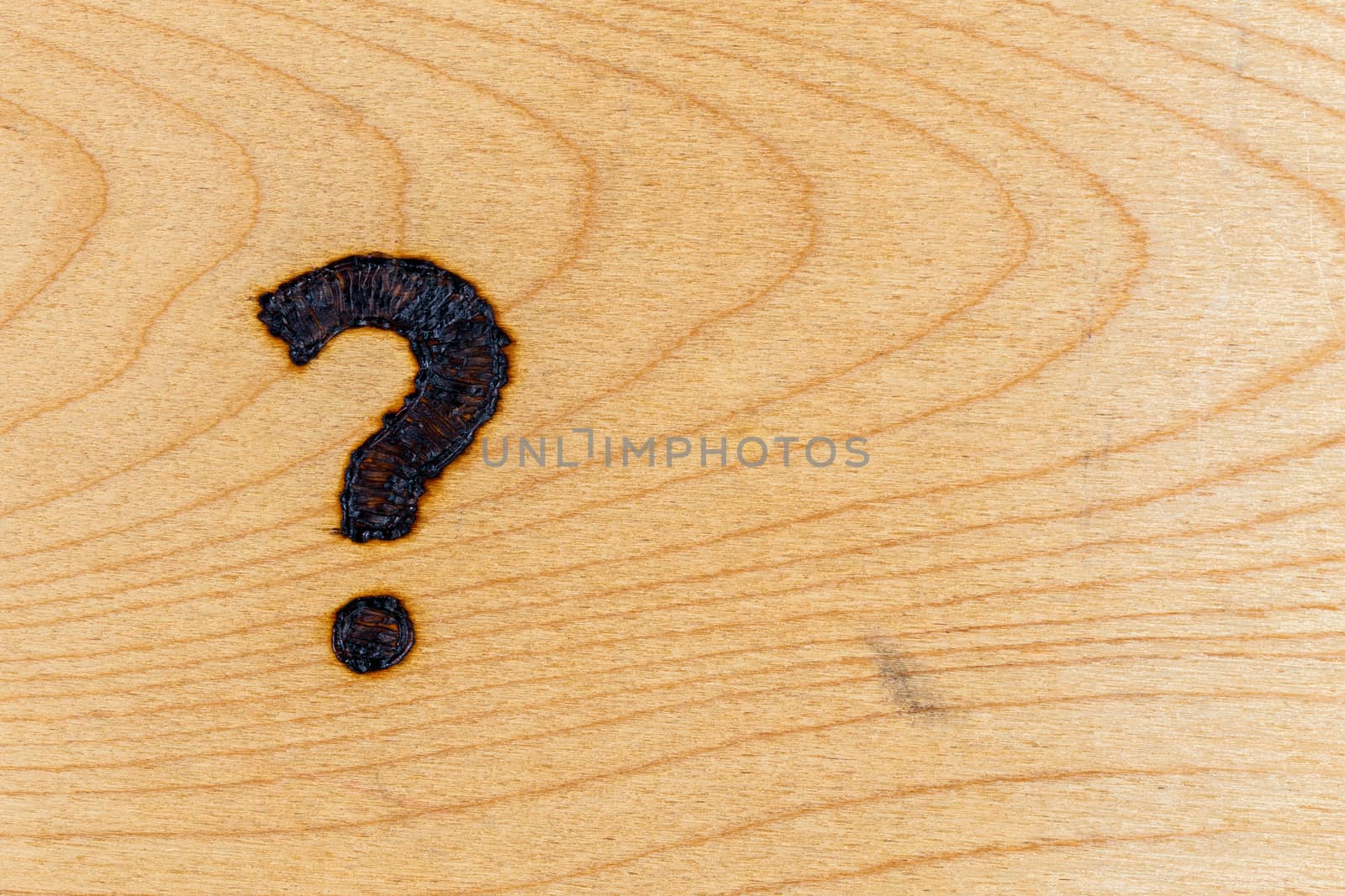question mark handwritten with handheld woodburner on bright flat wooden surface by z1b