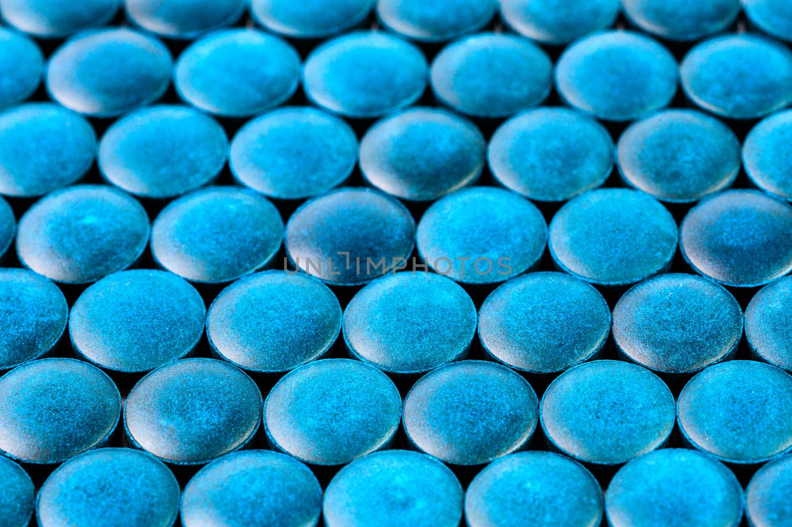 close-up background of many blue organic spirulina tablets laid tight in one layer on flat surface.