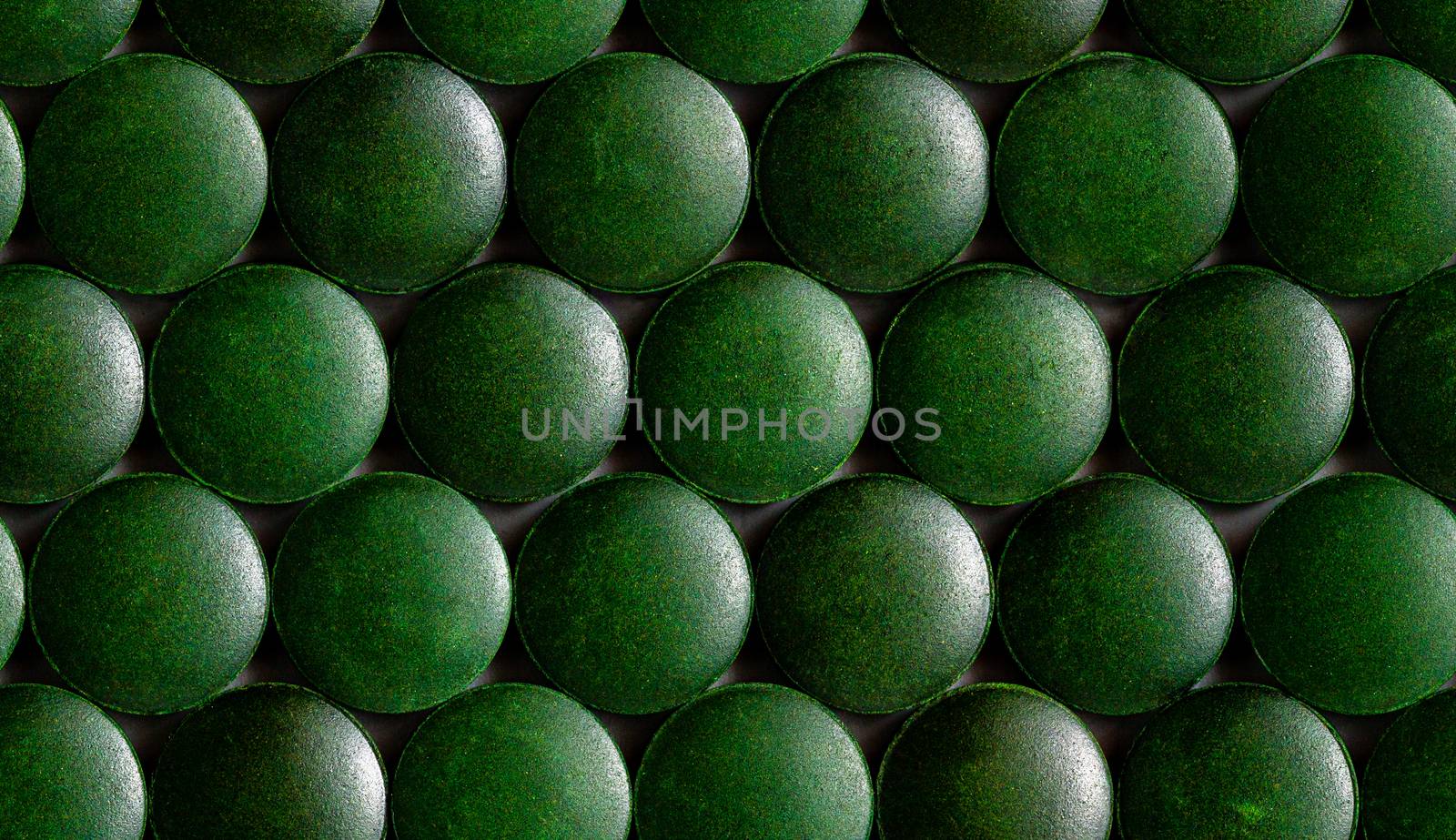 a seamless hexagonal pattern of many green organic spirulina tablets laid tight in one layer on flat surface.