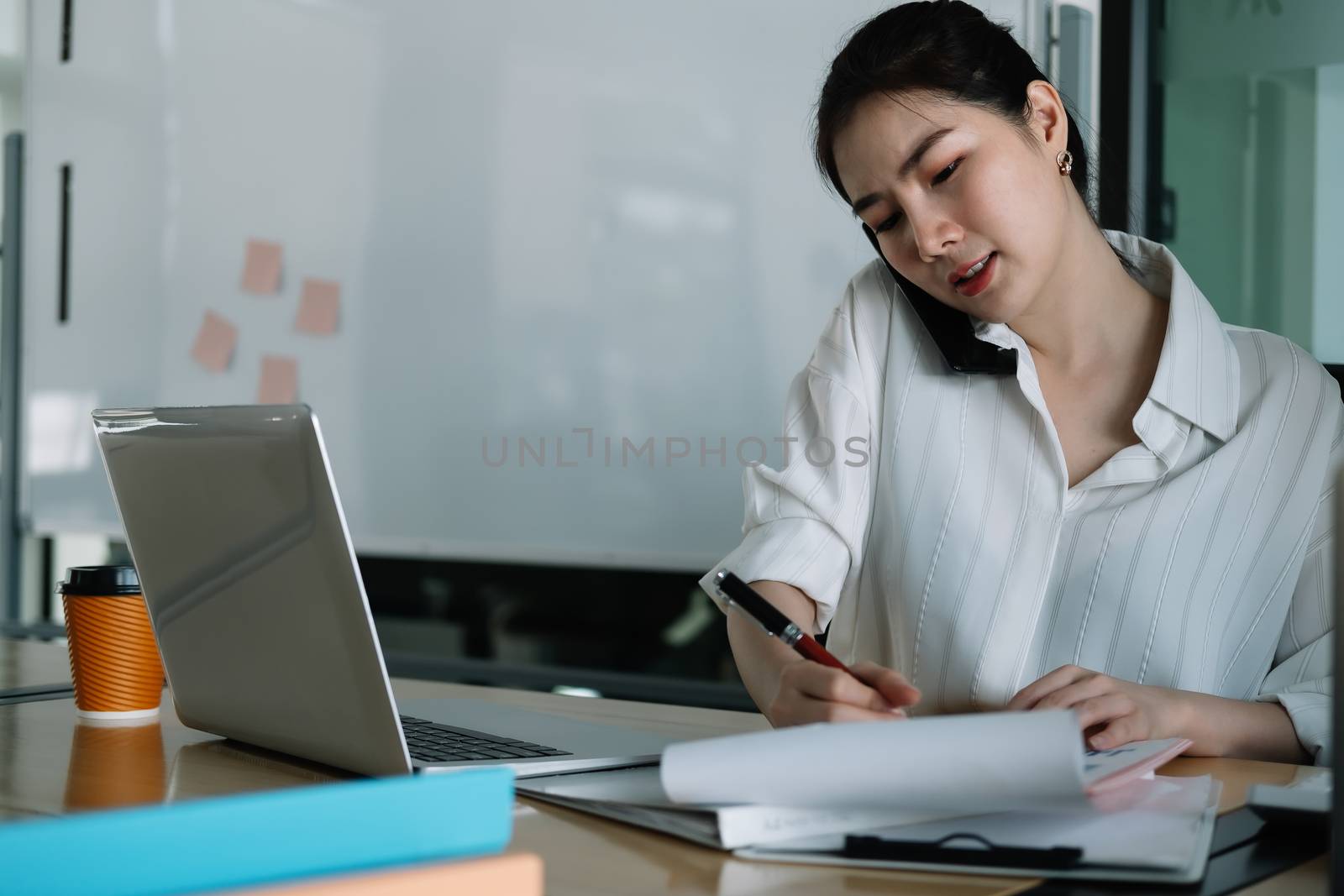 Young accountant hand holding smartphone to call marketing consultants and using laptop computer to analyze sales growth in the global workplace market. accounting concept