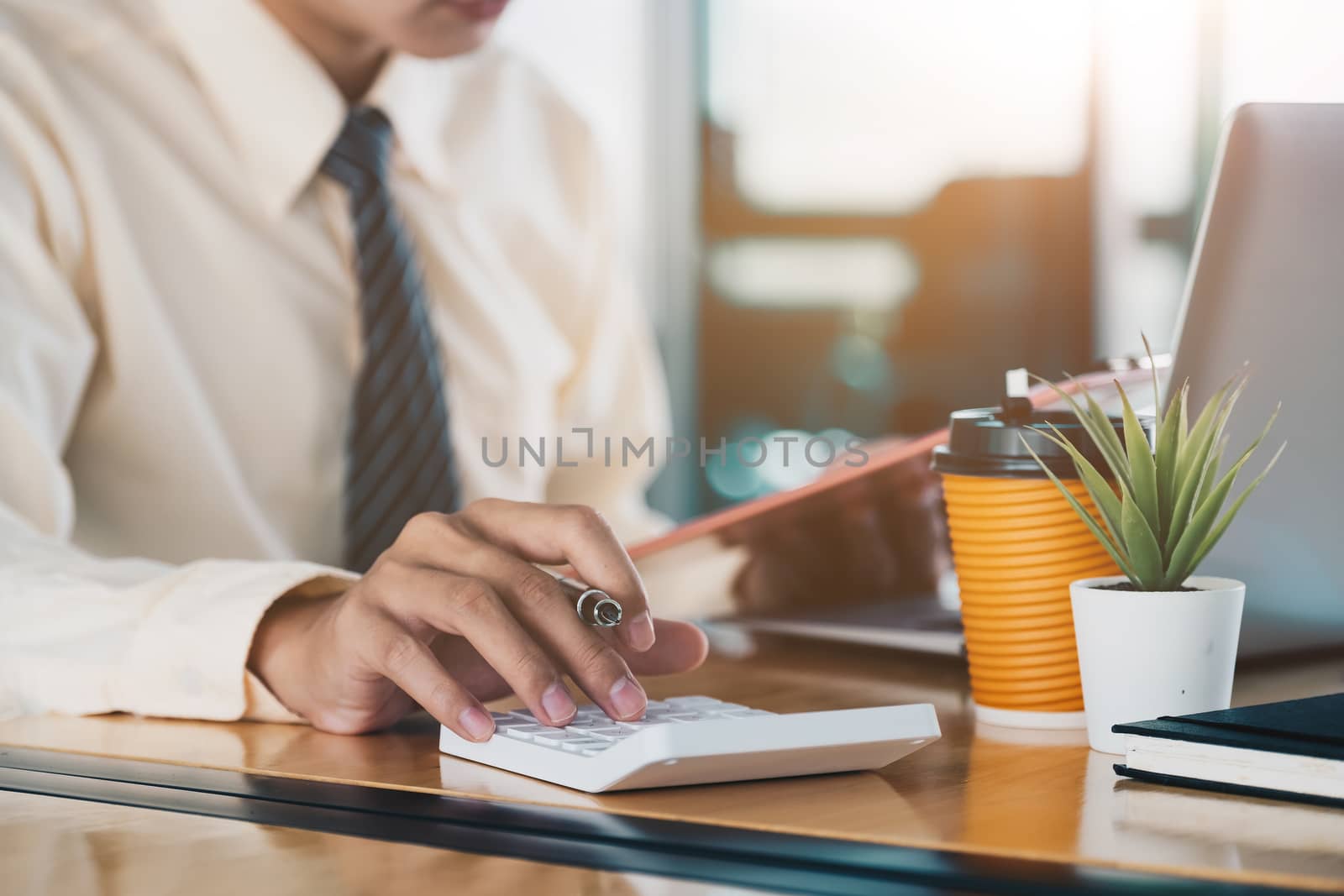 Close up of businessman or accountant hand holding pen working on calculator to calculate business data, accountancy document and laptop computer at office, business concept.