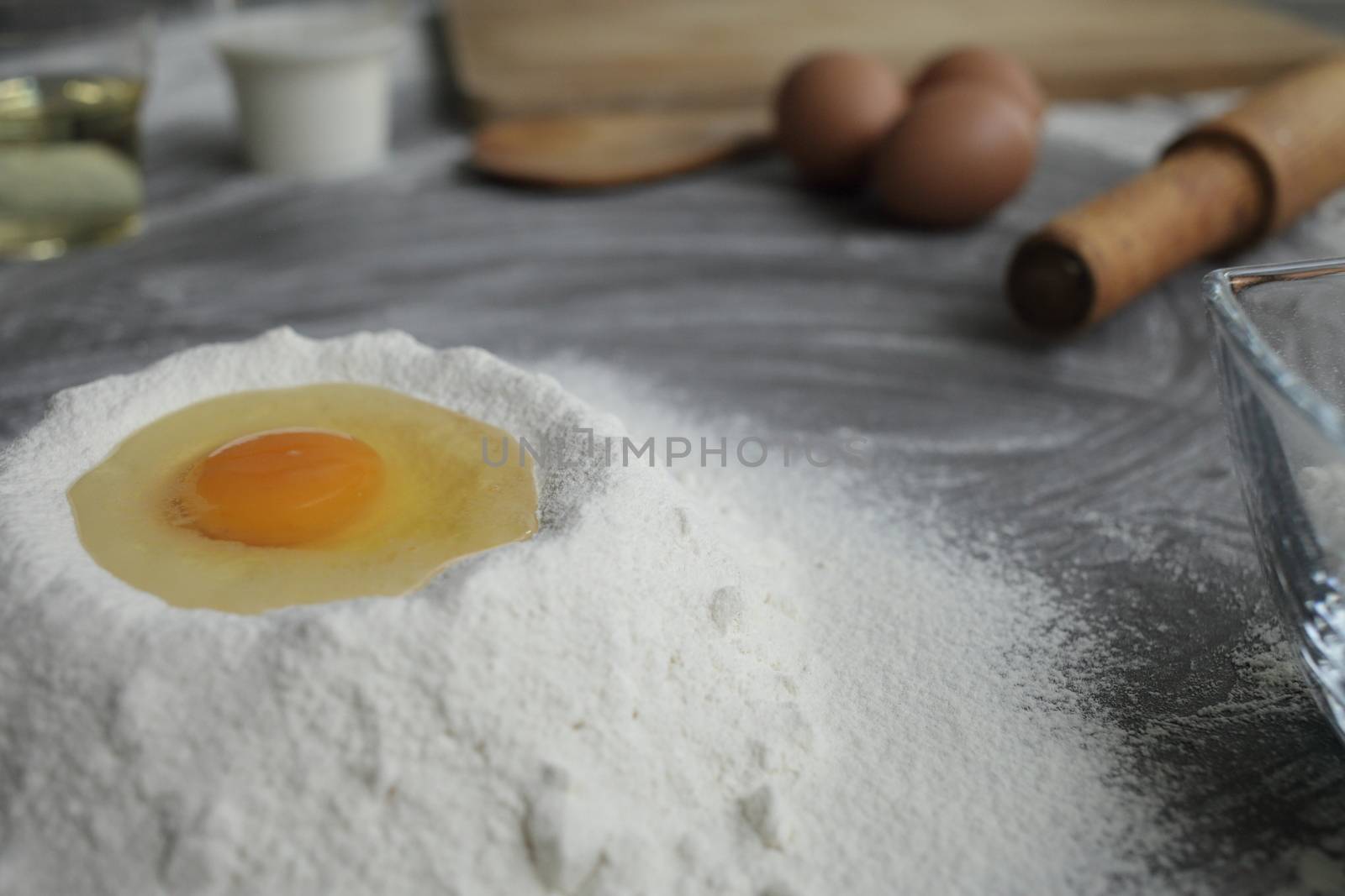 Broken chicken egg in a pile of flour, olive oil, milk, kitchen tool, gray table by selinsmo