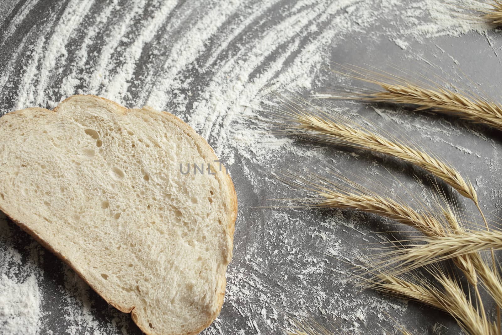 Wheat ears, a slice of bread, flour on a gray table background. View from above. Ears of wheat and flour on a gray background. Top view, grain. Ripe wheat. For baking bread. High quality photo