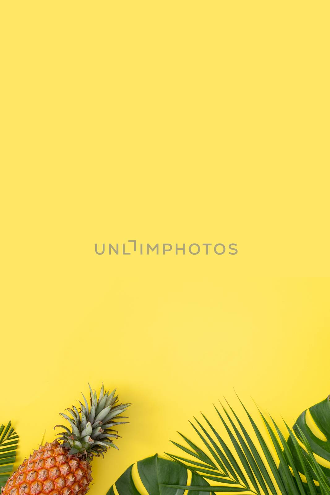 Beautiful pineapple on tropical palm monstera leaves isolated on bright pastel yellow background, top view, flat lay, overhead above summer fruit.