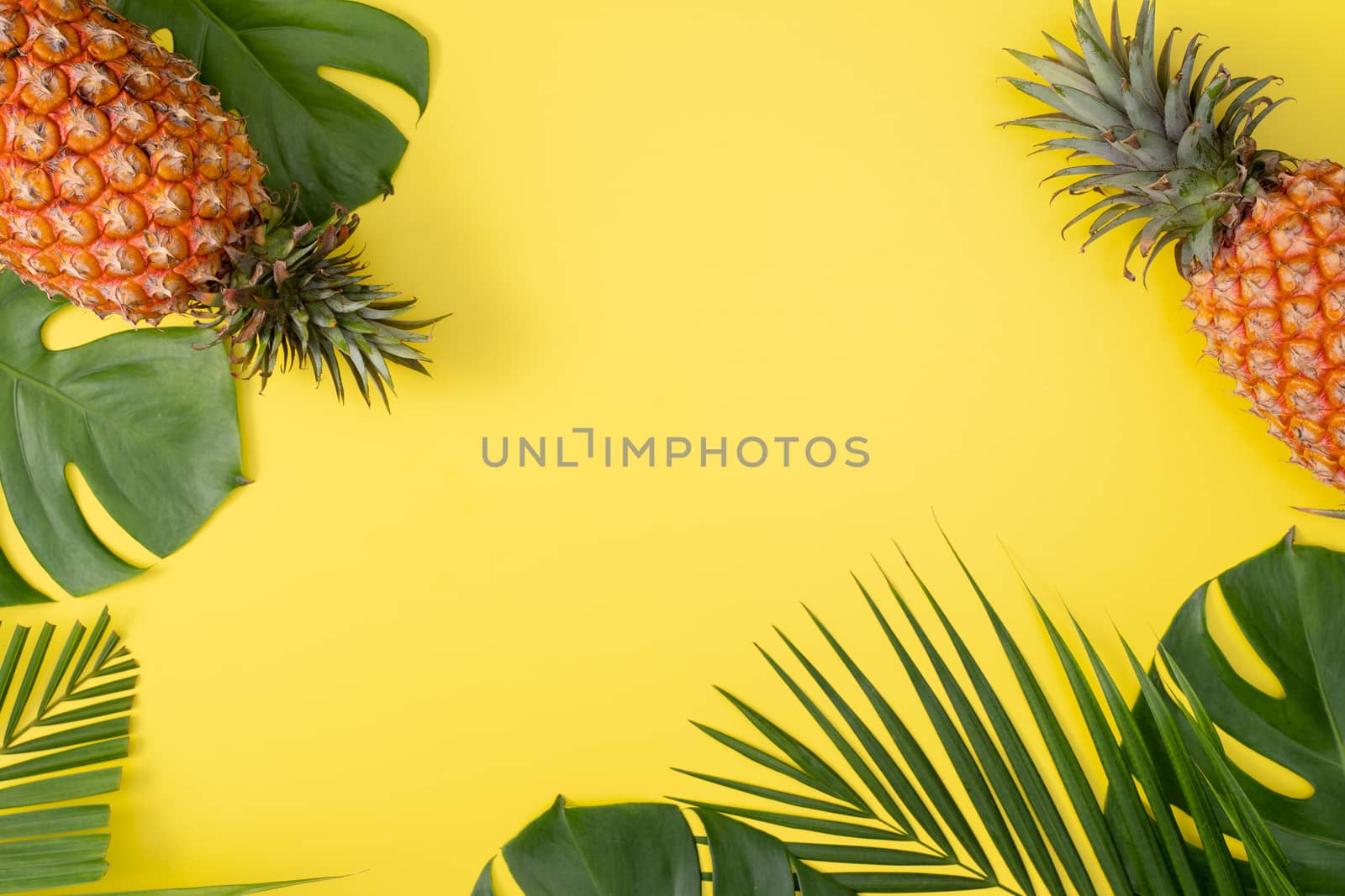 Beautiful pineapple on tropical palm monstera leaves isolated on bright pastel yellow background, top view, flat lay, overhead above summer fruit.