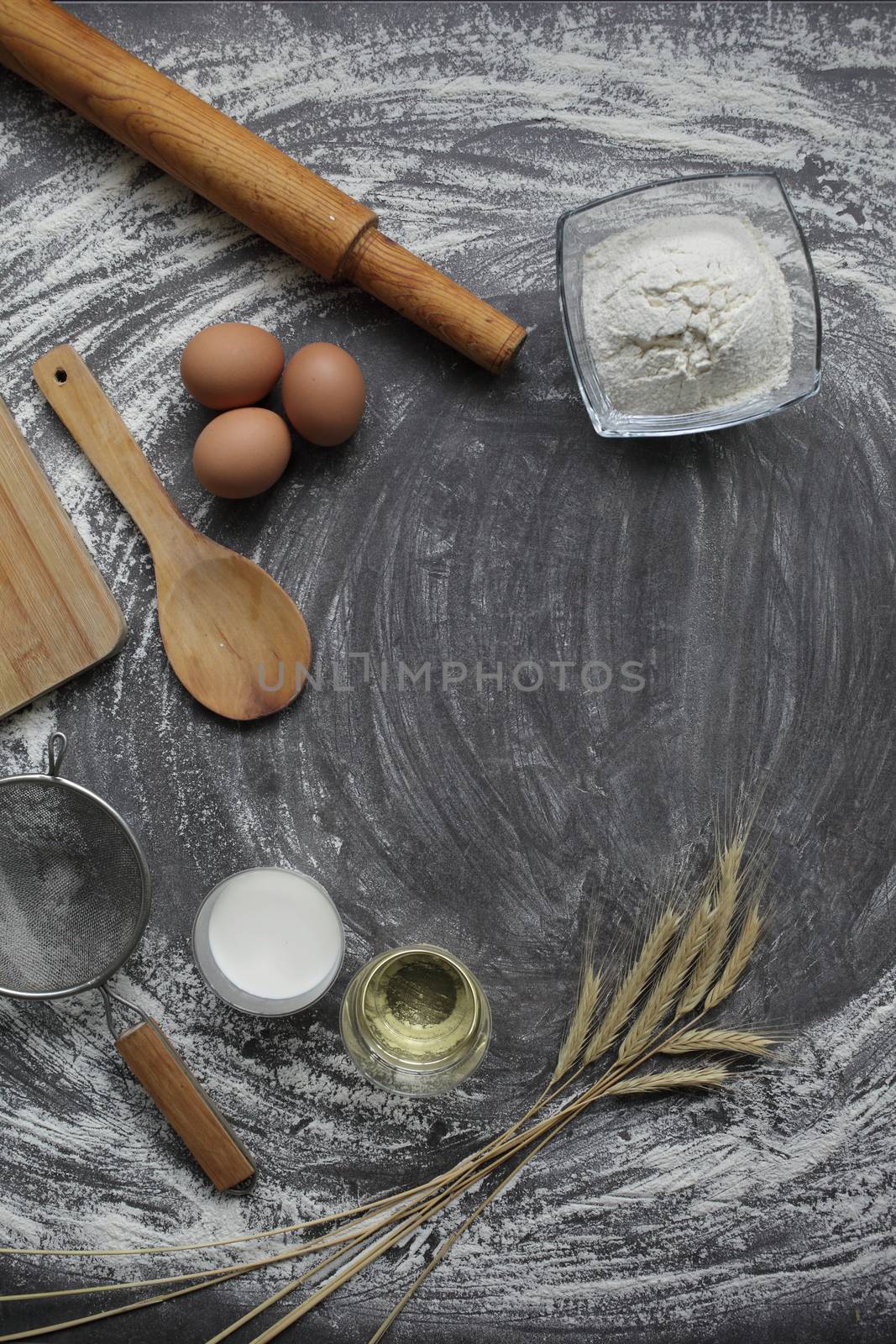 Chicken egg, flour, olive oil, milk, wheat ears, kitchen tool on gray table background. Products for baking bakery products. Cutting board, rolling pin, flour sieve, wooden spoon. For bread or cake