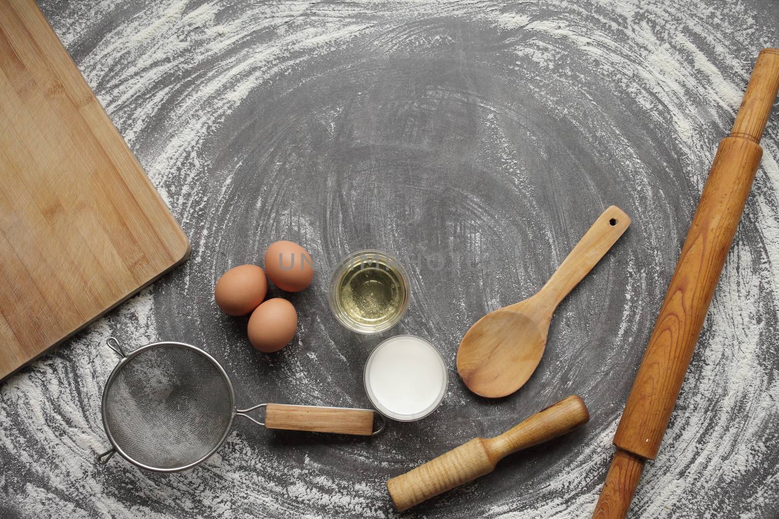 Chicken egg, flour, olive oil, milk, kitchen tool on gray table background. Products for baking bakery products. Cutting board, rolling pin, flour sieve, wooden spoon. For bread or cake
