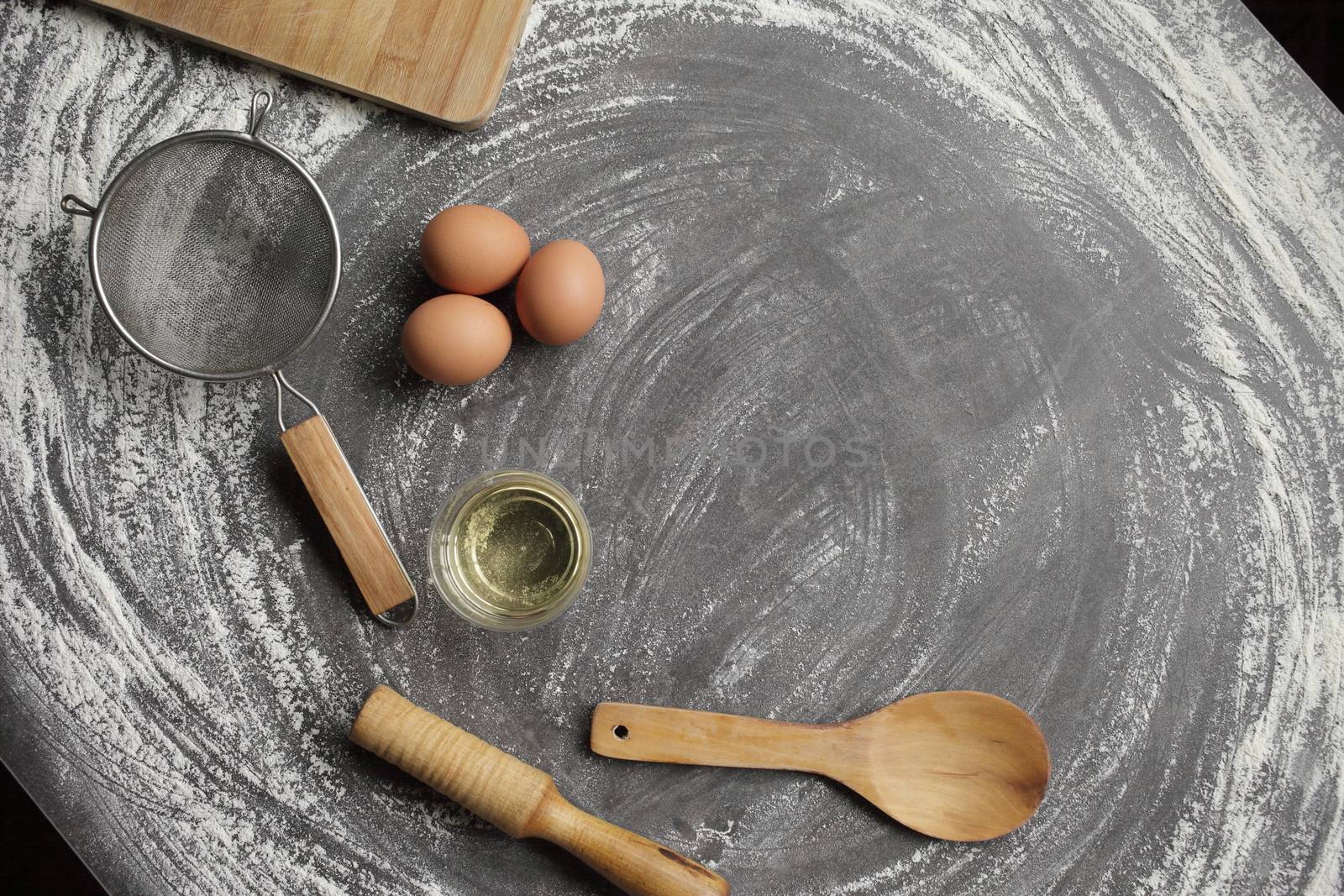 Chicken egg, flour, olive oil, kitchen tool on gray table background. Products for baking bakery products. Cutting board, rolling pin, flour sieve, wooden spoon. For bread or cake