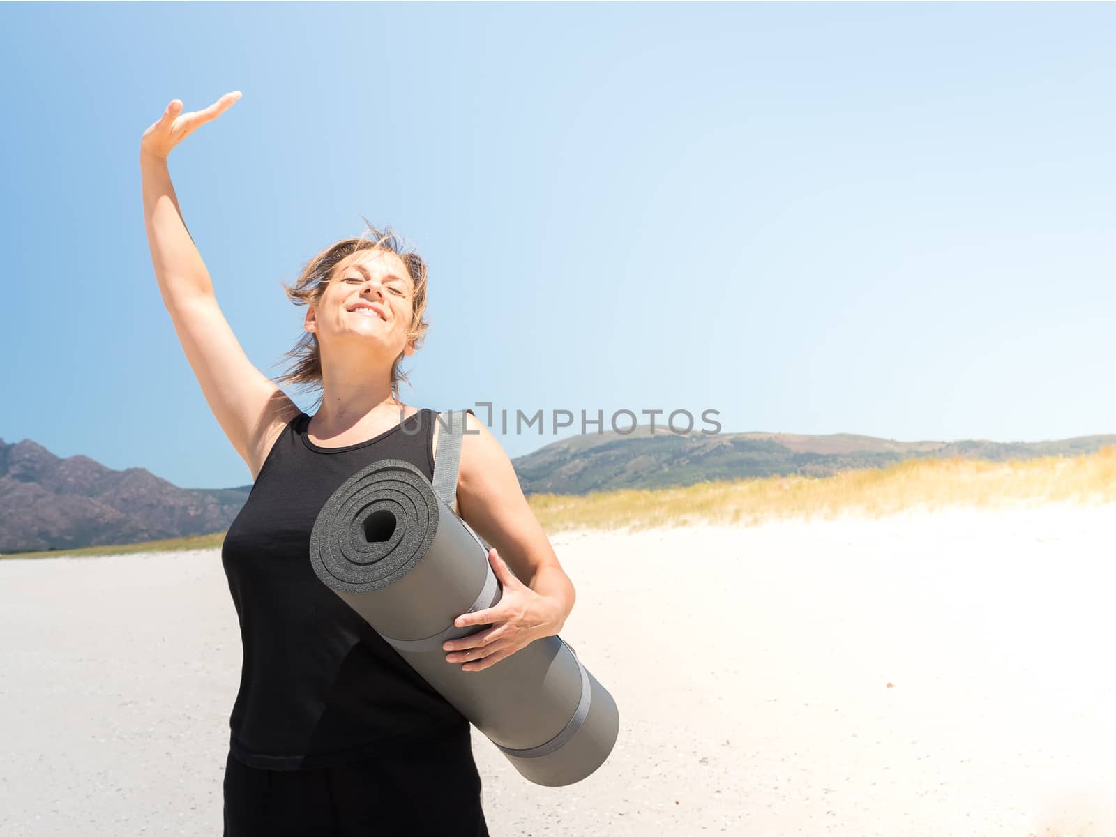 Woman in sportswear enjoying at the beach with a rolled-up mat under her arm . Copy space.