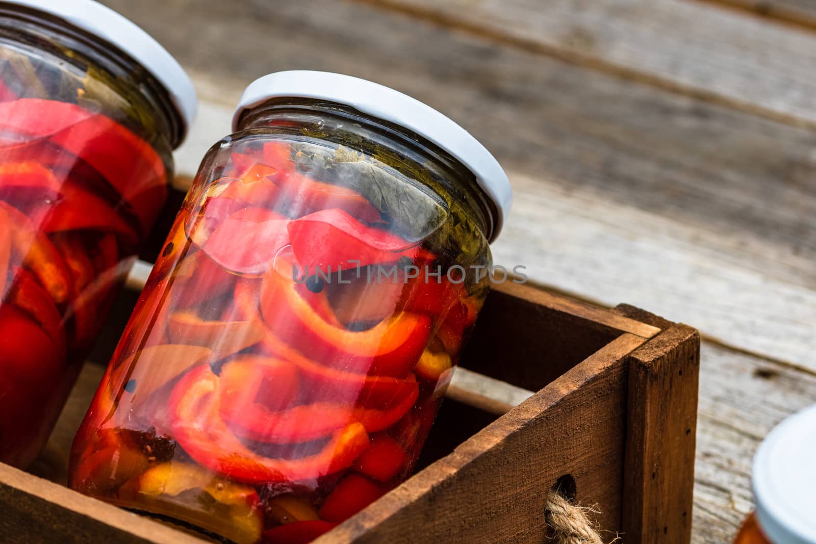 Wooden crate with glass jars with pickled red bell peppers.Preserved food concept, canned vegetables isolated in a rustic composition.