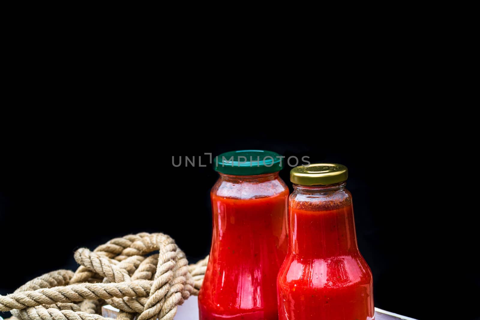 Bottles with tomatoes sauce isolated on black in a rustic composition.