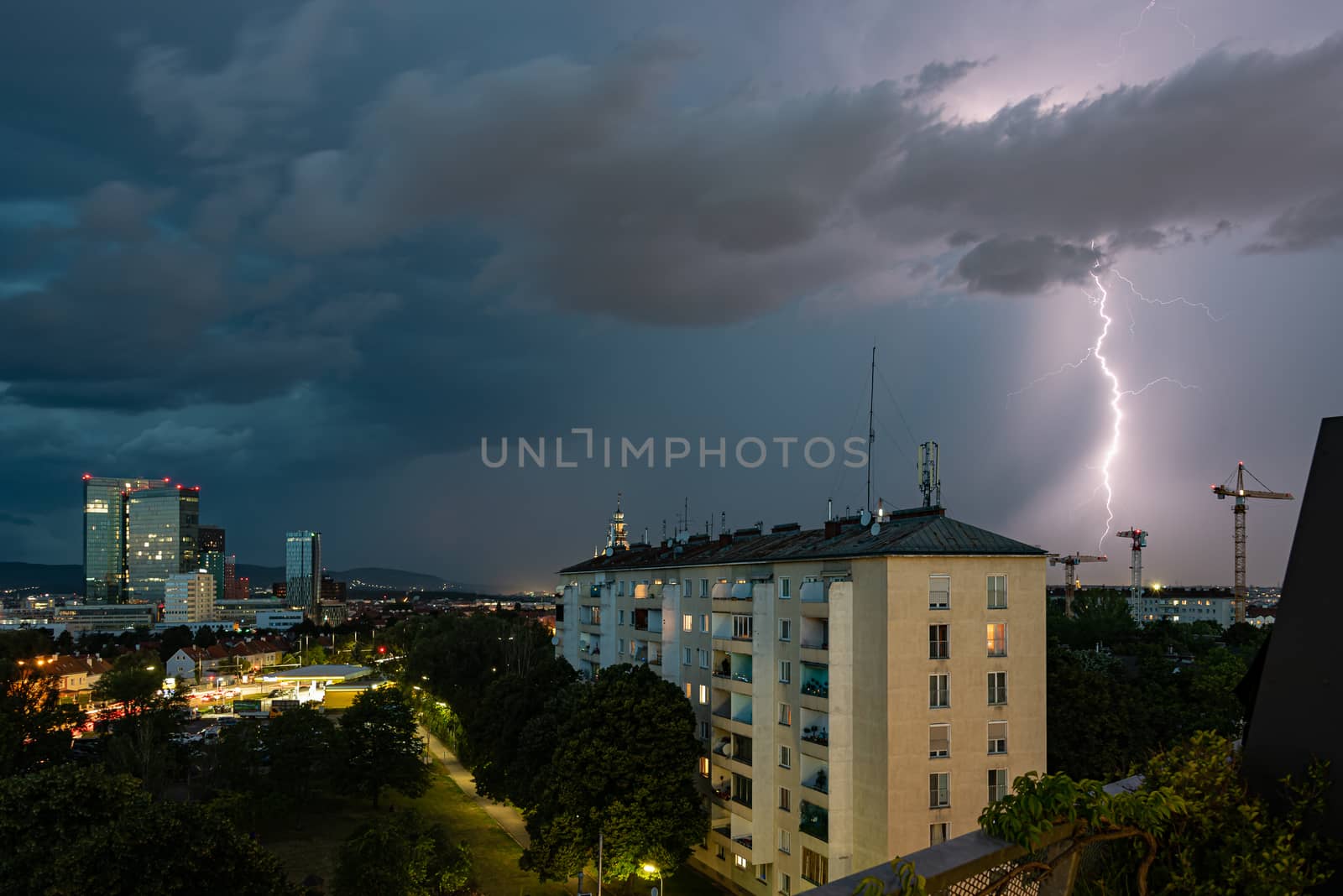 Violent summer thunderstorm with enormous lightning over the Wienerberg City in Vienna with construction cranes on the right side of the picture