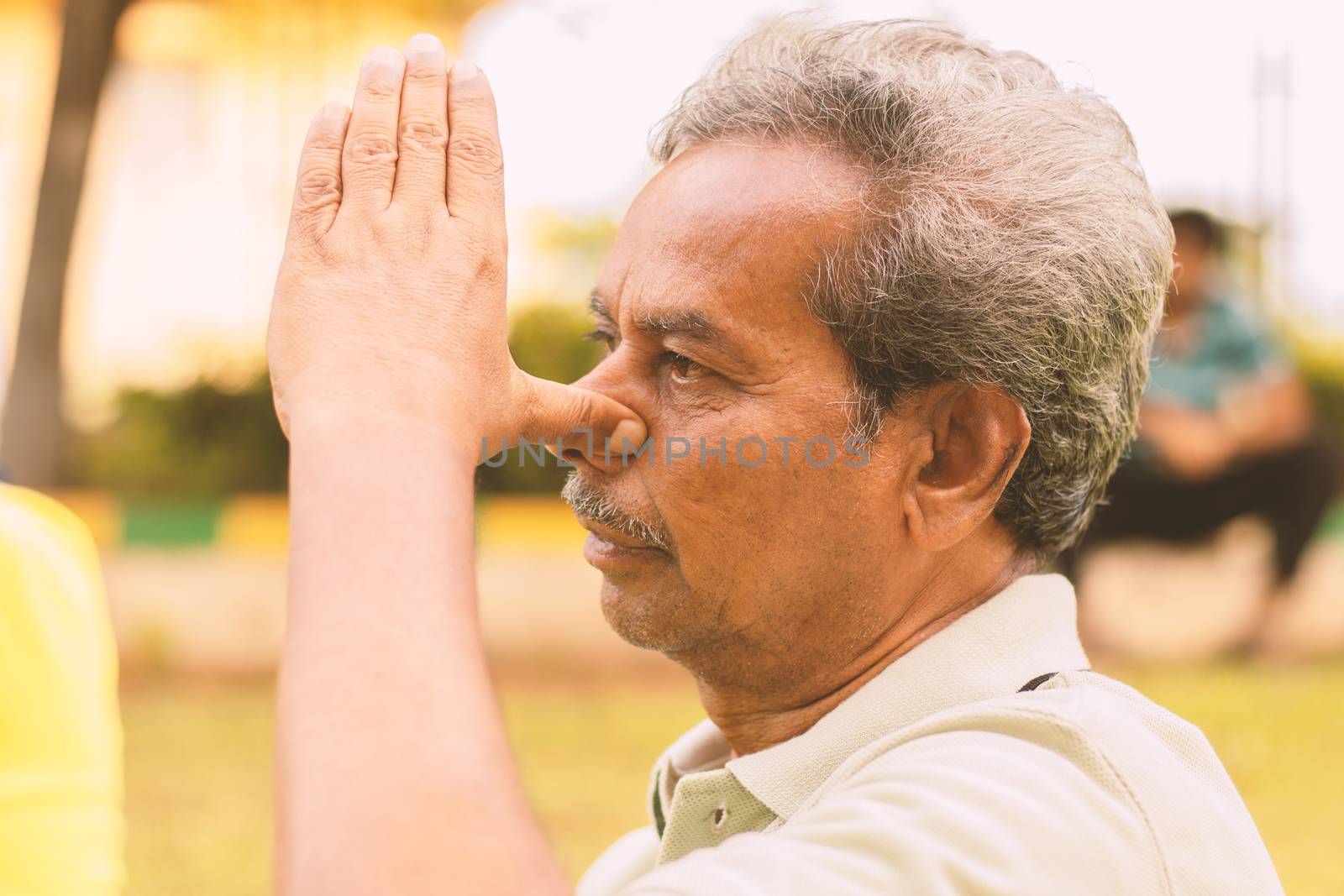 Closeup of of senior man doing alternate Nostril Breathing exercise or nadi shodhana pranayama at park - Concept of healthy active old people lifestyle