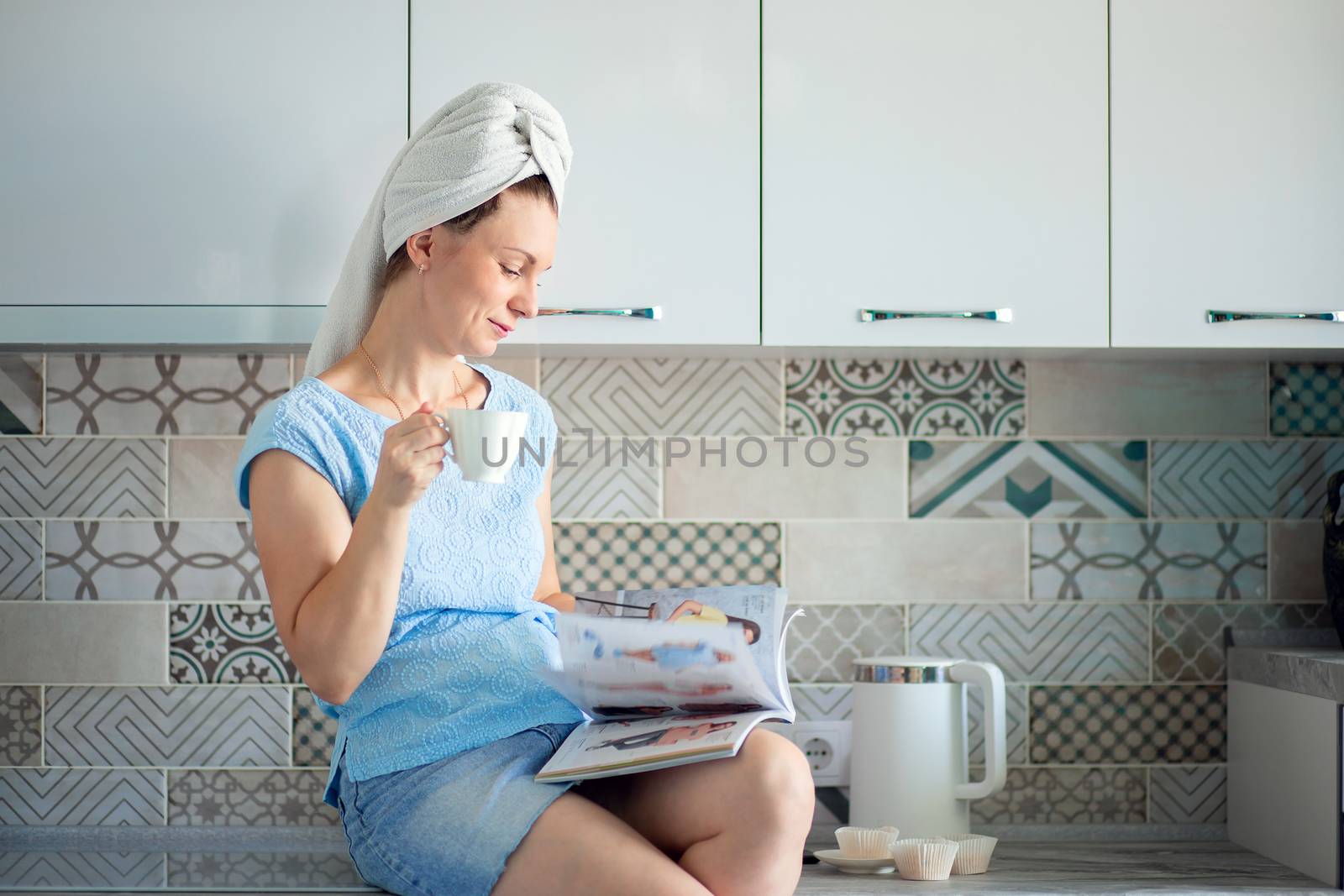Woman with a towel on her head in her kitchen having breakfast and leafing through a magazine
