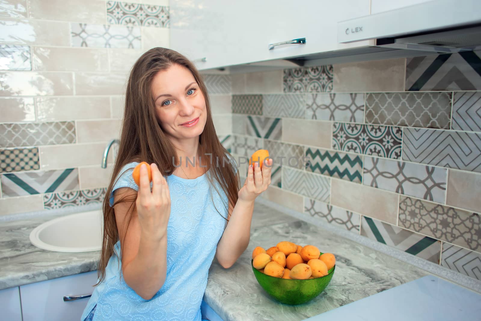 A girl with long hair at home in the kitchen sorts out ripe apricots