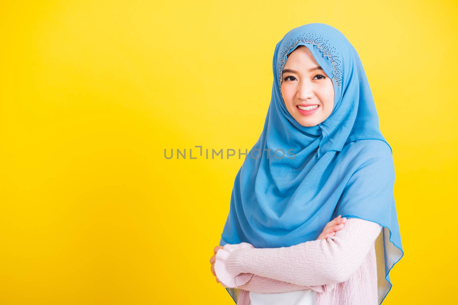 Asian Muslim Arab, Portrait of happy beautiful young woman Islamic religious wear veil hijab she smiling stand crossed arm, studio shot isolated on yellow background