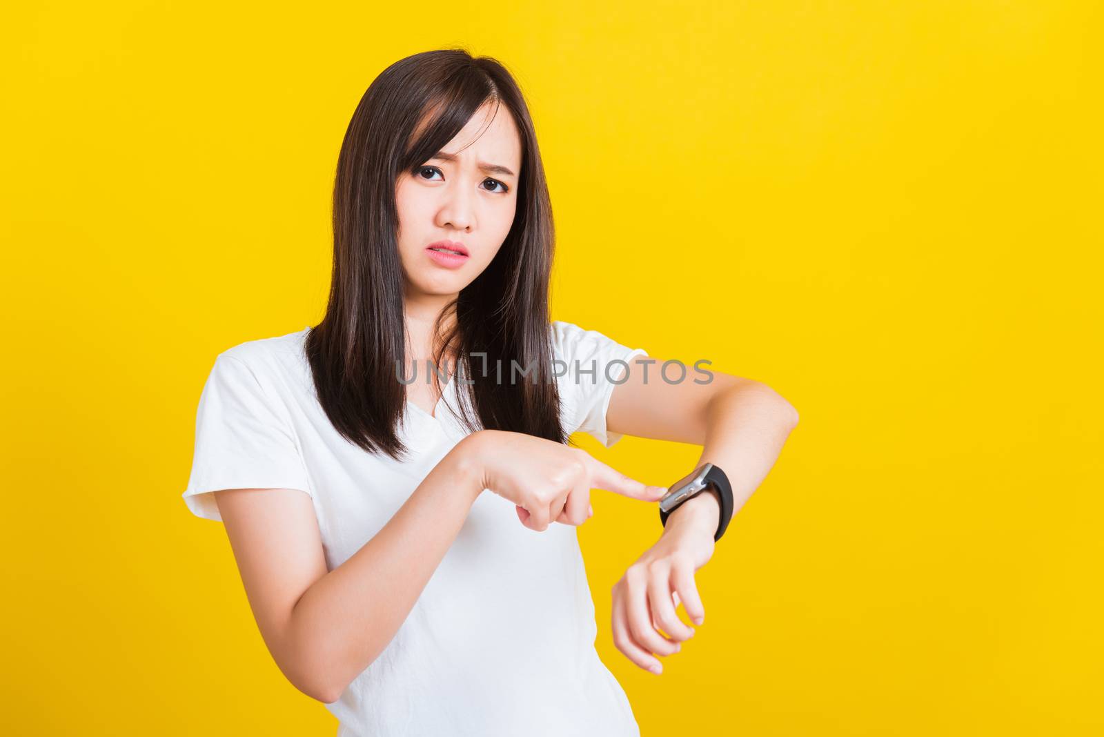 You are late not on time, Portrait Asian of a happy beautiful young woman scared casual girl showing and pointing finger her wristwatch studio shot isolated on yellow background