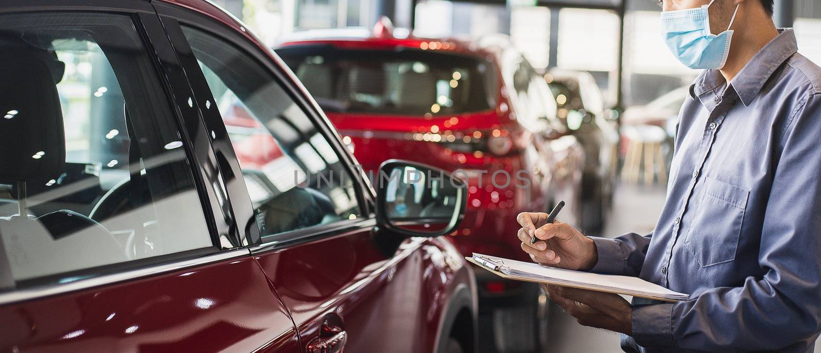 Asian saleman wear surgical mask working in inspector checking writing on clipboard in garage of dealership Wait mechanic In showroom car and insurance new normol covid-19 in showroom dealership