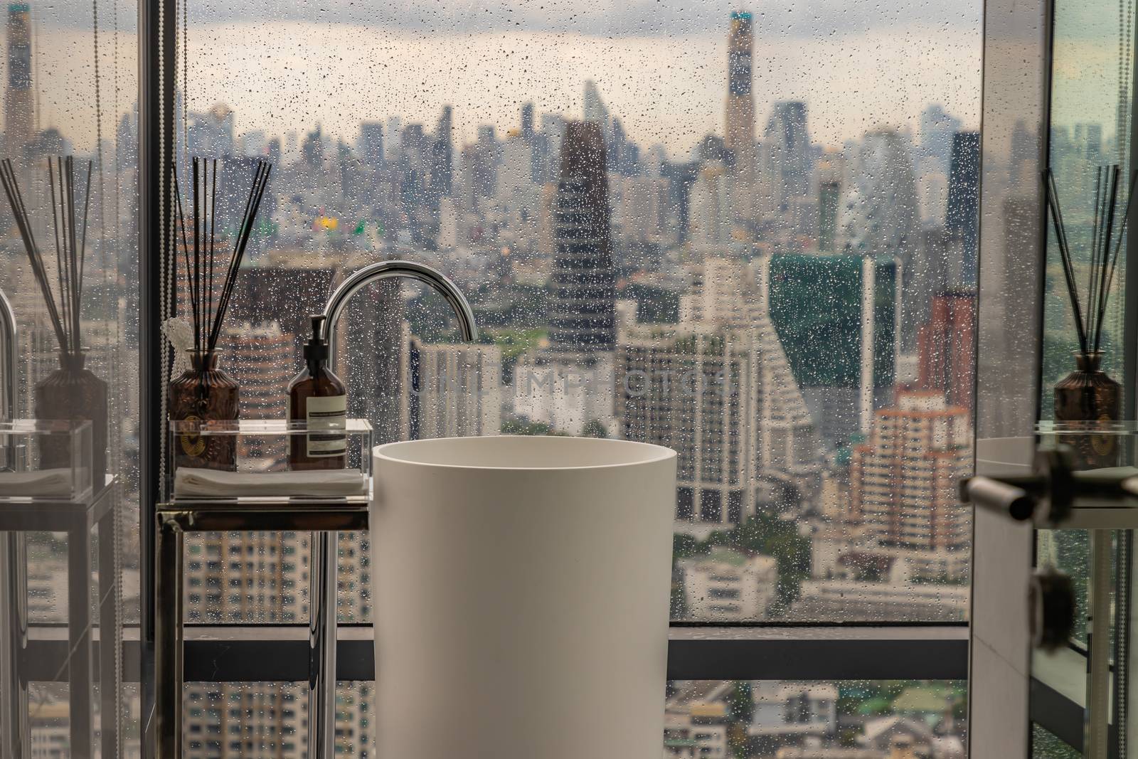 Modern white restroom with cityscape that can look outside from big window on a rainy day. Elegant faucets and components, Sanitary ware, The concept of health care. Selective focus.