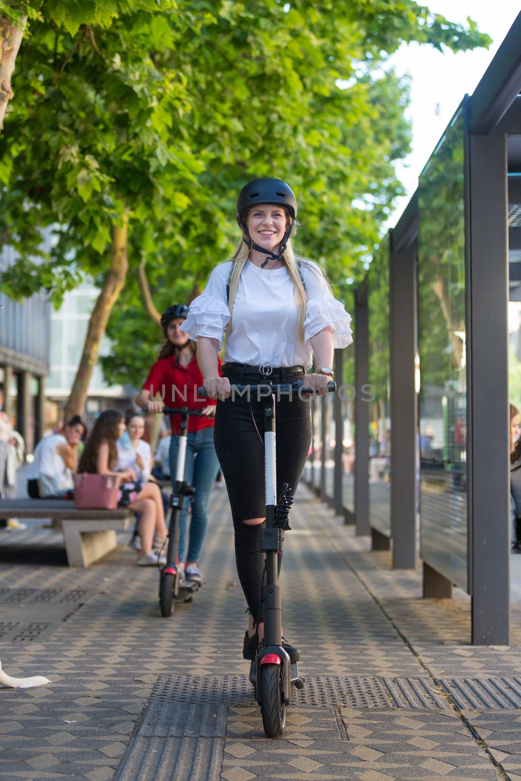 Trendy fashinable teenager girls riding public rental electric scooters in urban city environment. New eco-friendly modern public city transport in Ljubljana, Slovenia by kasto