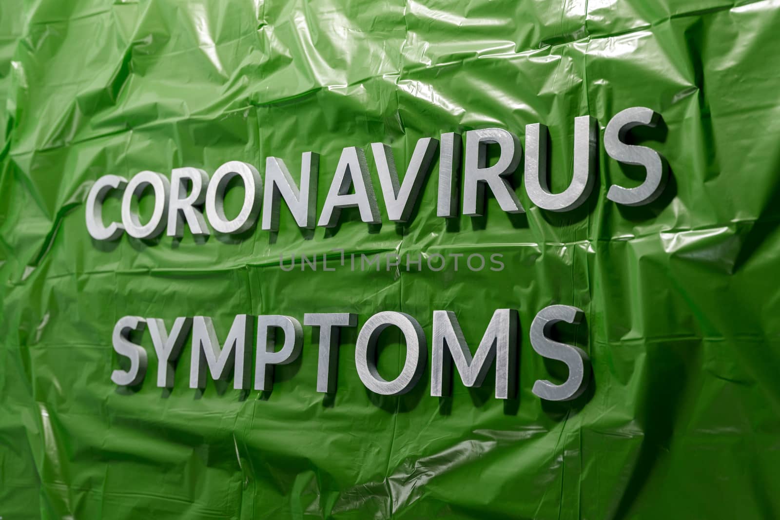 the words coronavirus symptoms laid with silver letters on crumpled green plastic film - linear perspective composition with selective focus and dramatic light