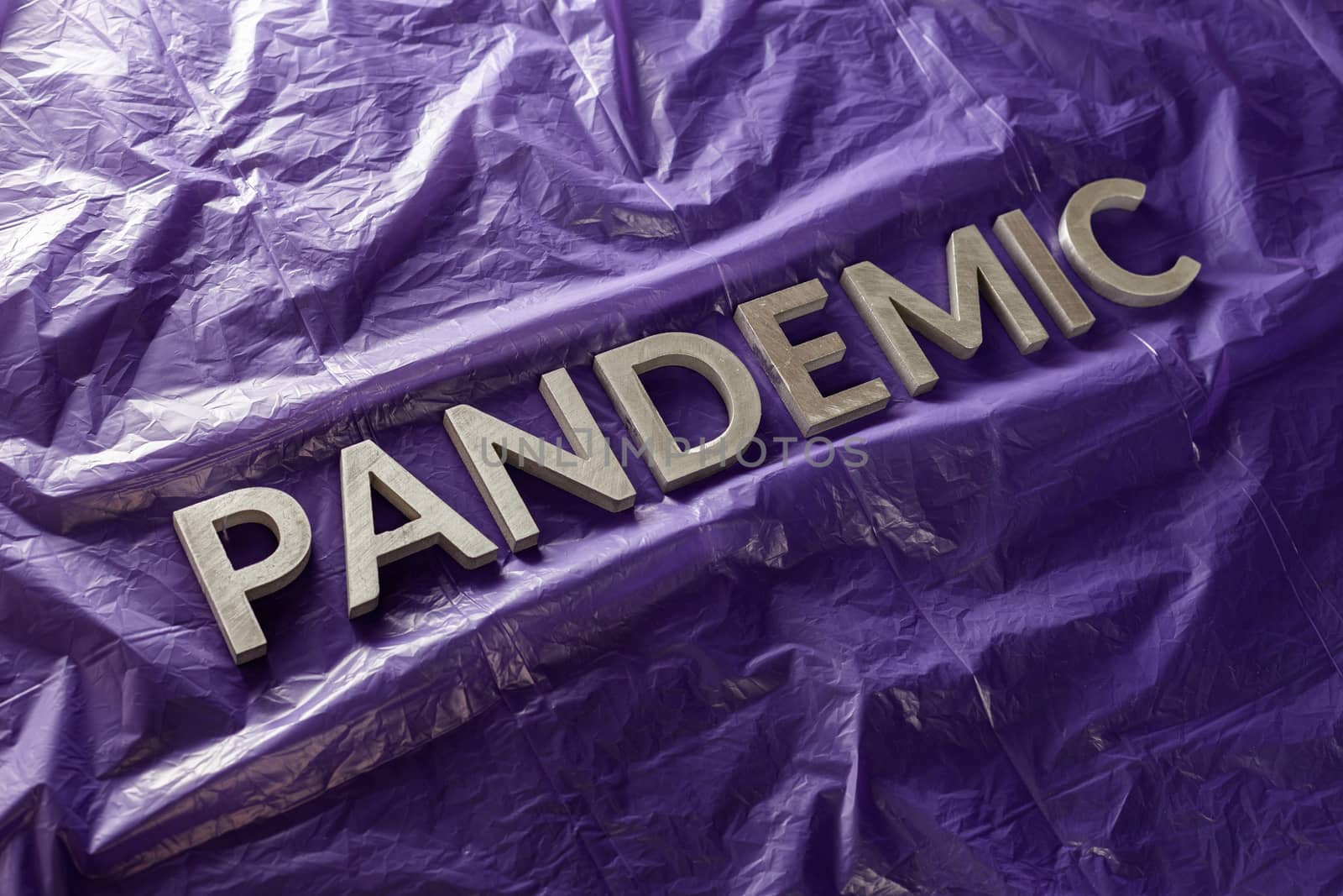 the word pandemic laid with silver metal letters on crumpled violet protective plastic film background in slanted diagonal perspective by z1b