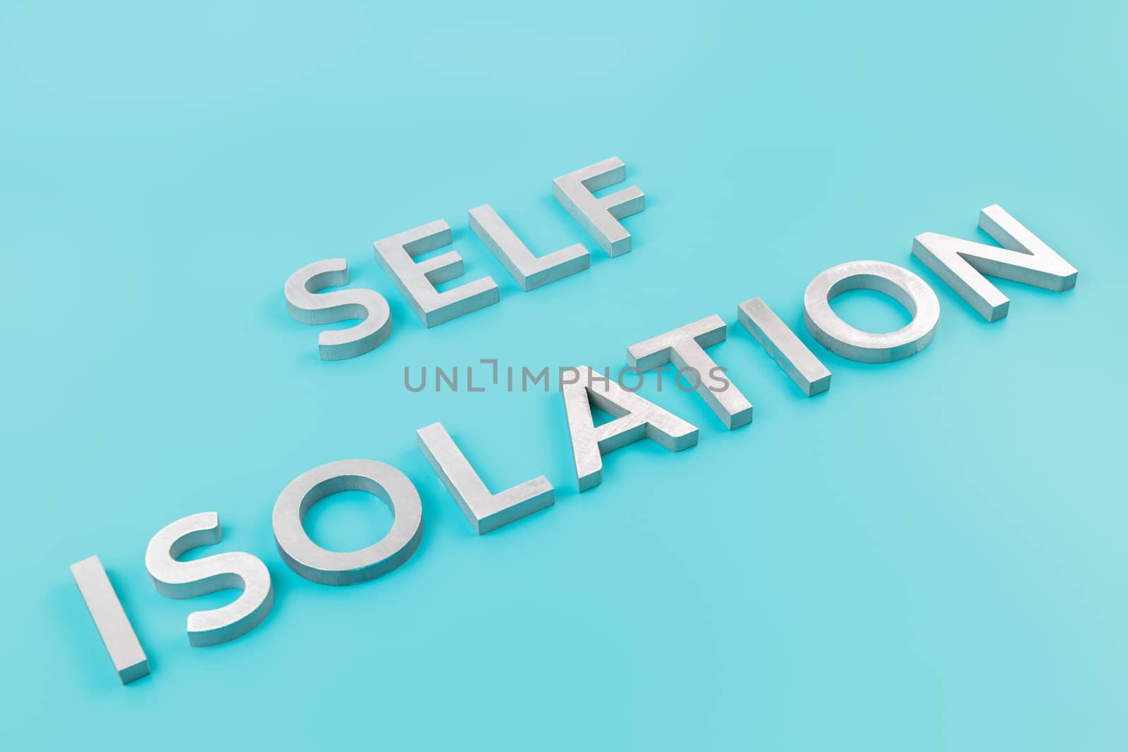 the words self isolation laid with silver metal letters on pastel blue background with diagonal slanted perspective with selective focus