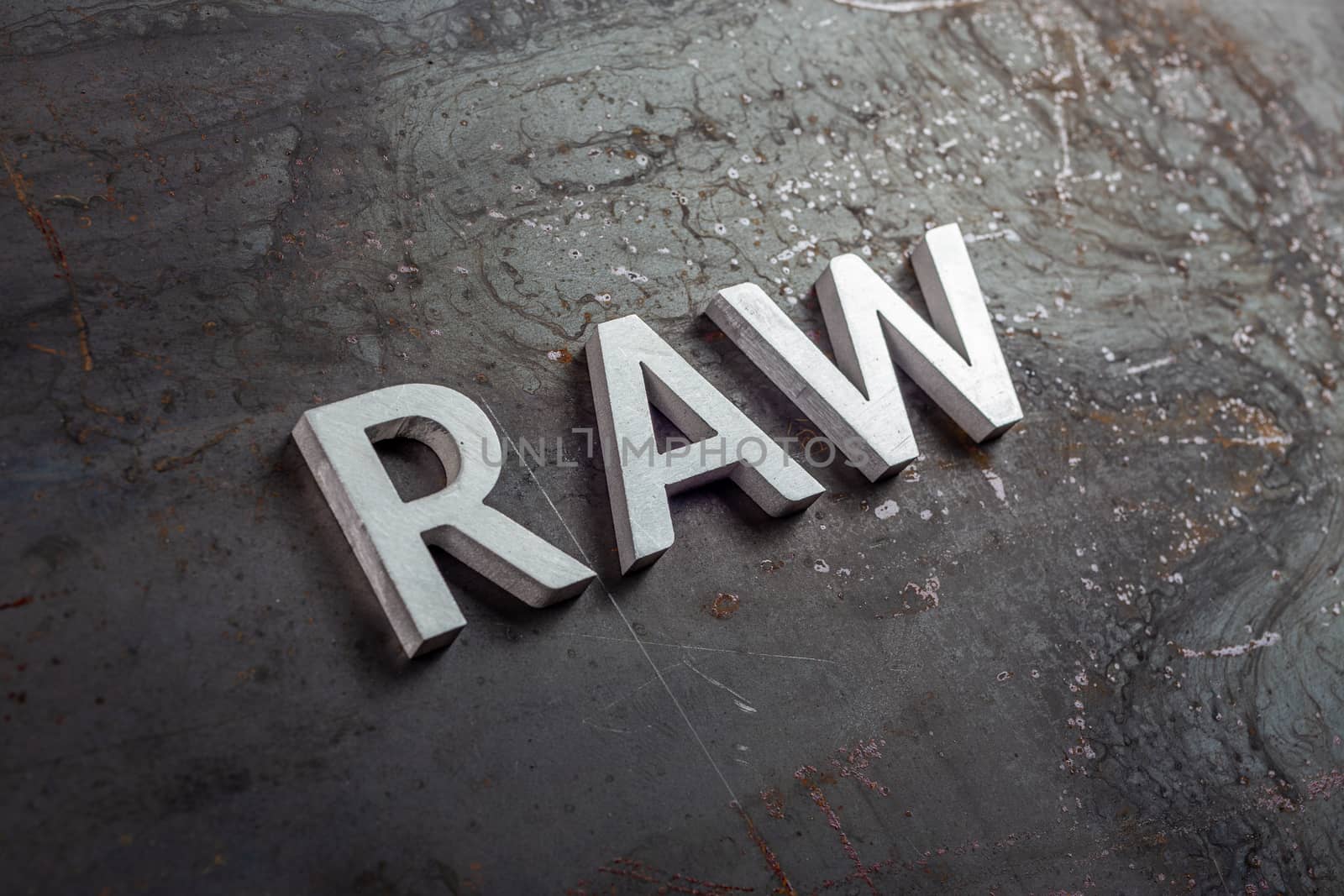 the word raw laid with silver metal letters on hot rolled steel sheet surface - close-up with selective focus and diagonal perspective