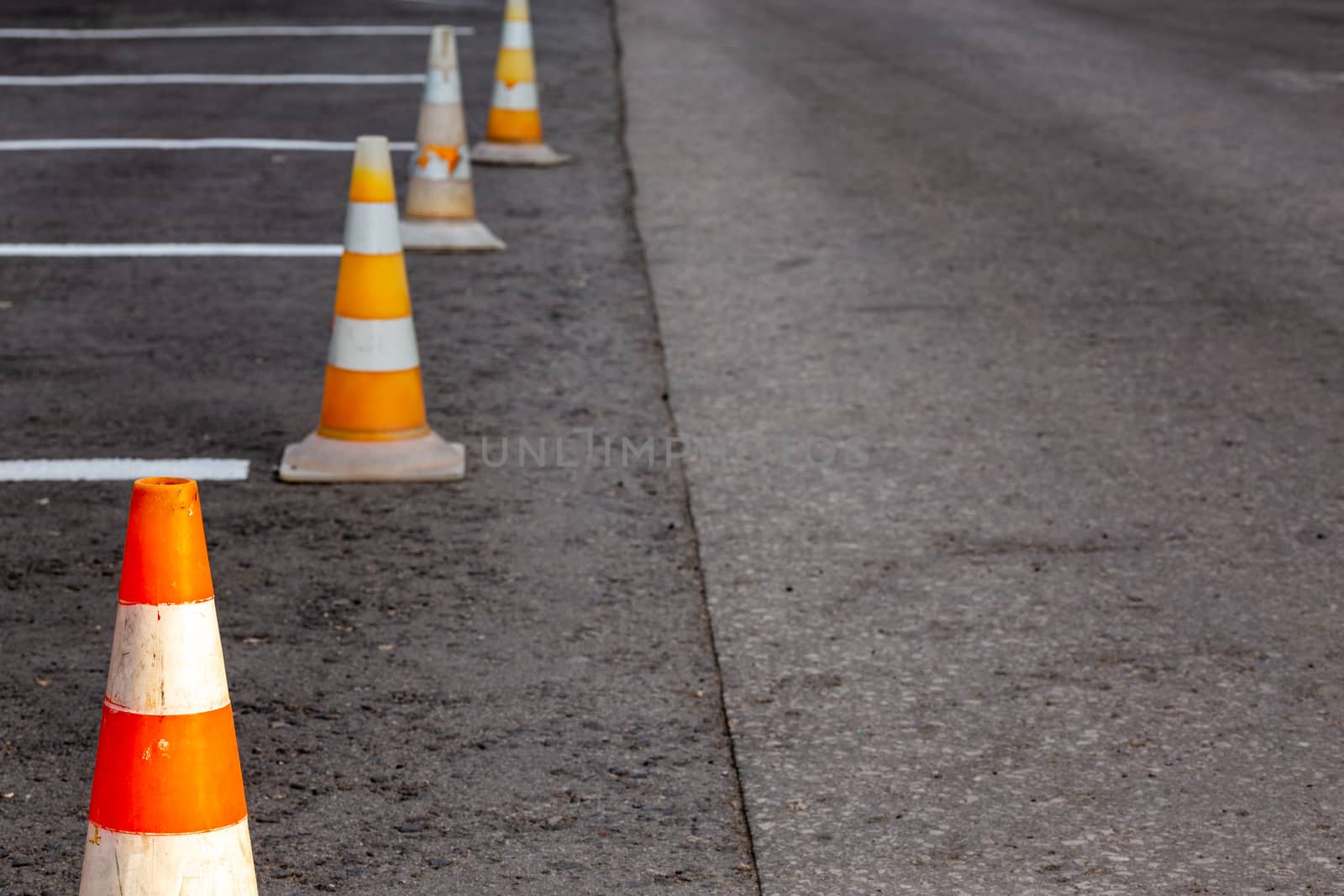 Orange road cones on a asphelt driving area with white lines, close-up with selective focus and backgropund blur.