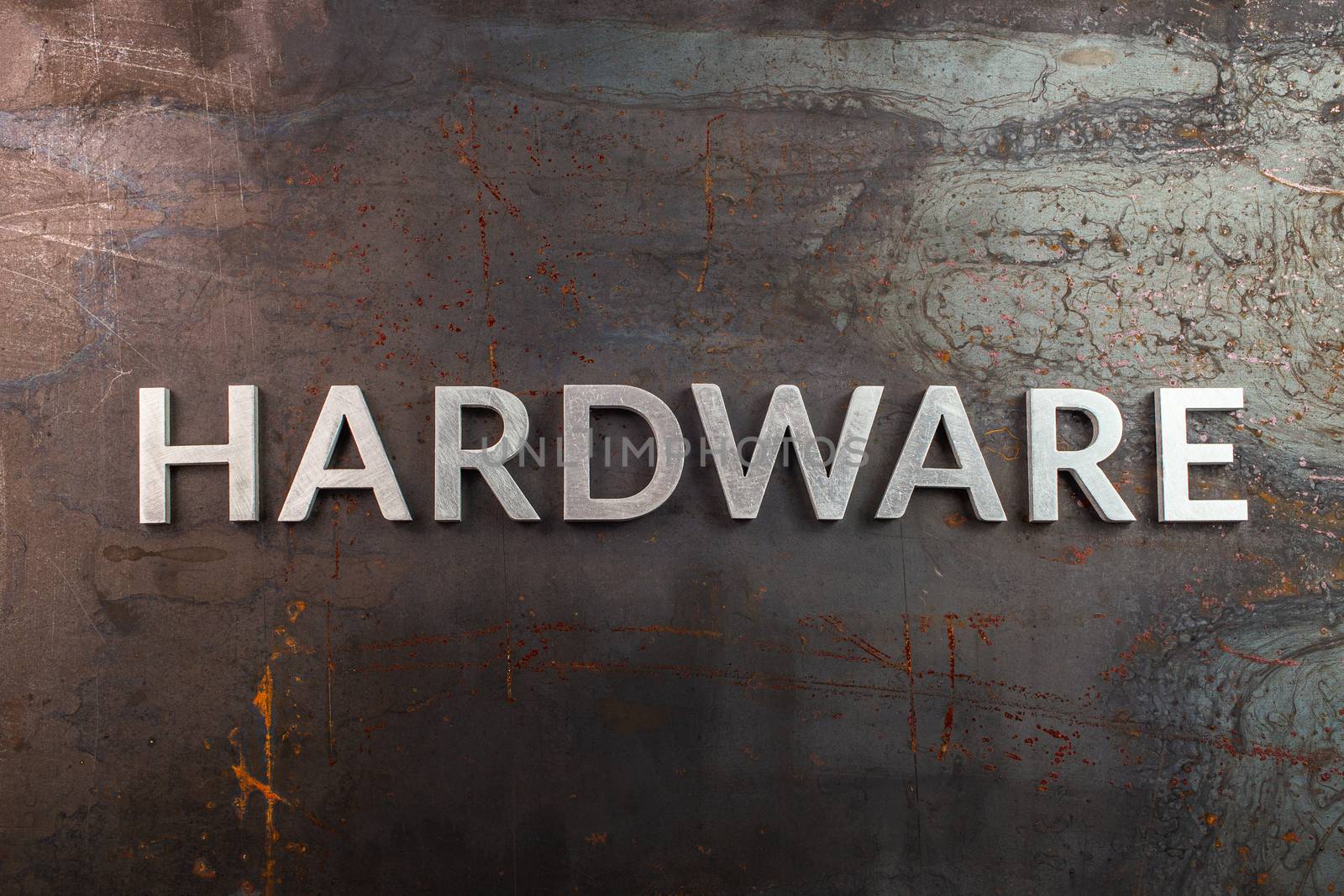 word hardware laid in with silver metal letters on rusted heavy hot rolled uncoated steel sheet surface - directly above in flat lay composition