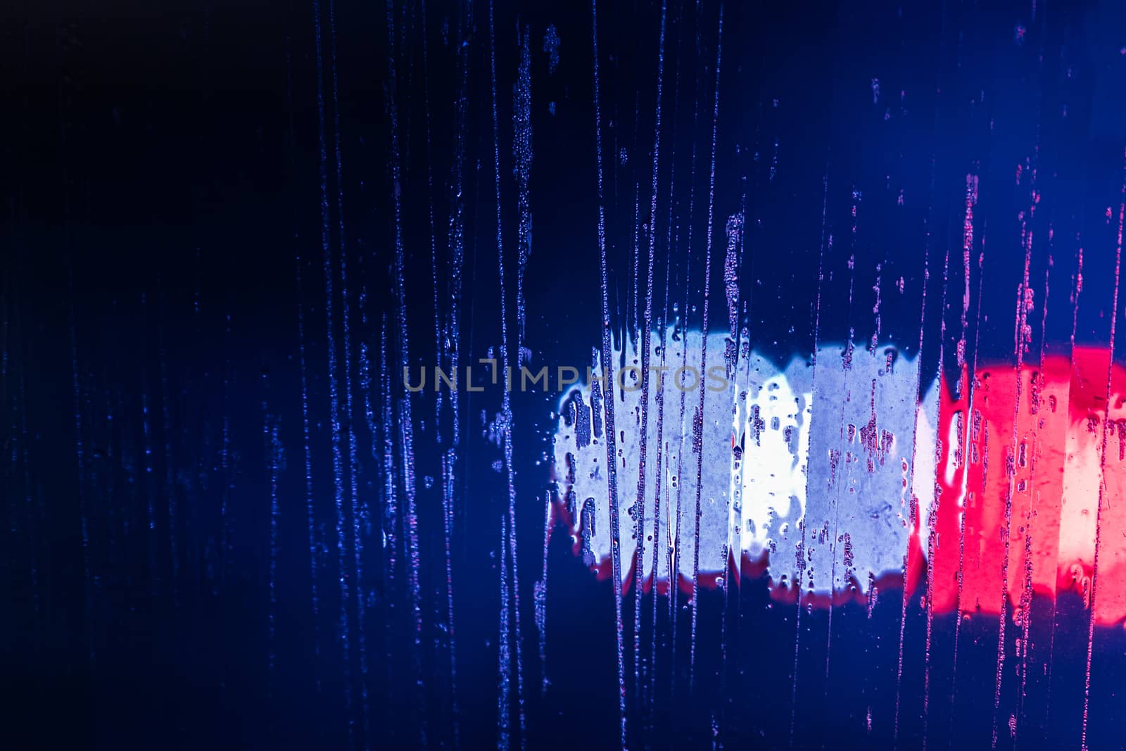 red and blue night police lights bokeh trough wet glass close-up with selective focus abstract background