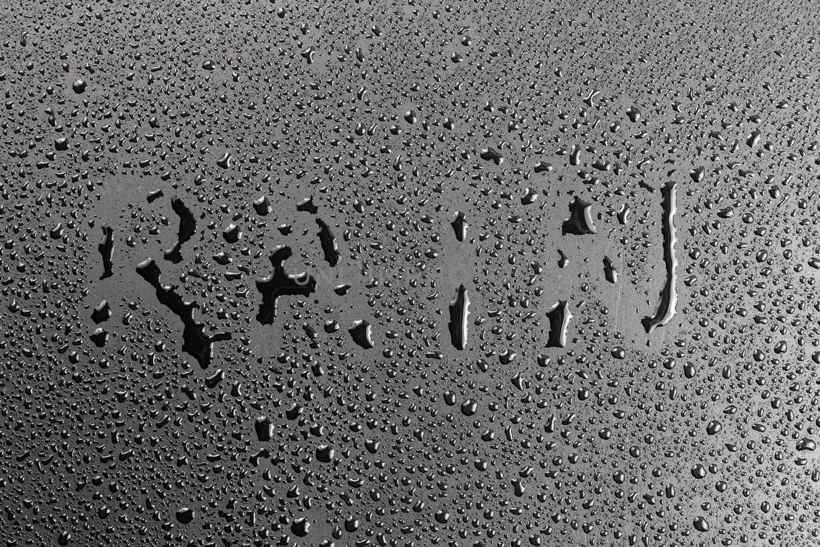 the word rain handwritten on matte black hydrophobic matte surface with water drops.